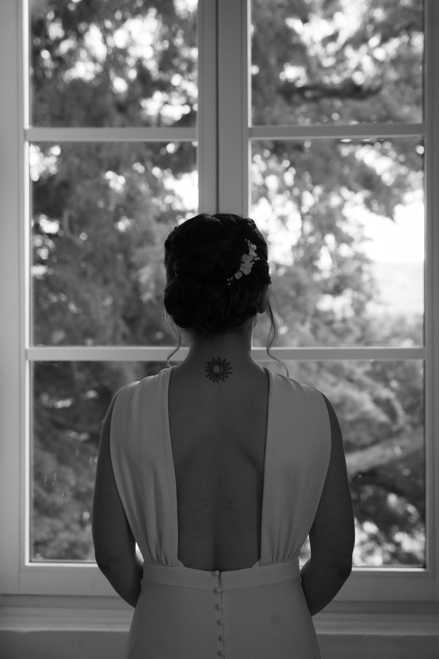 Back view of wedding dress showing tattoo and buttons against window light.