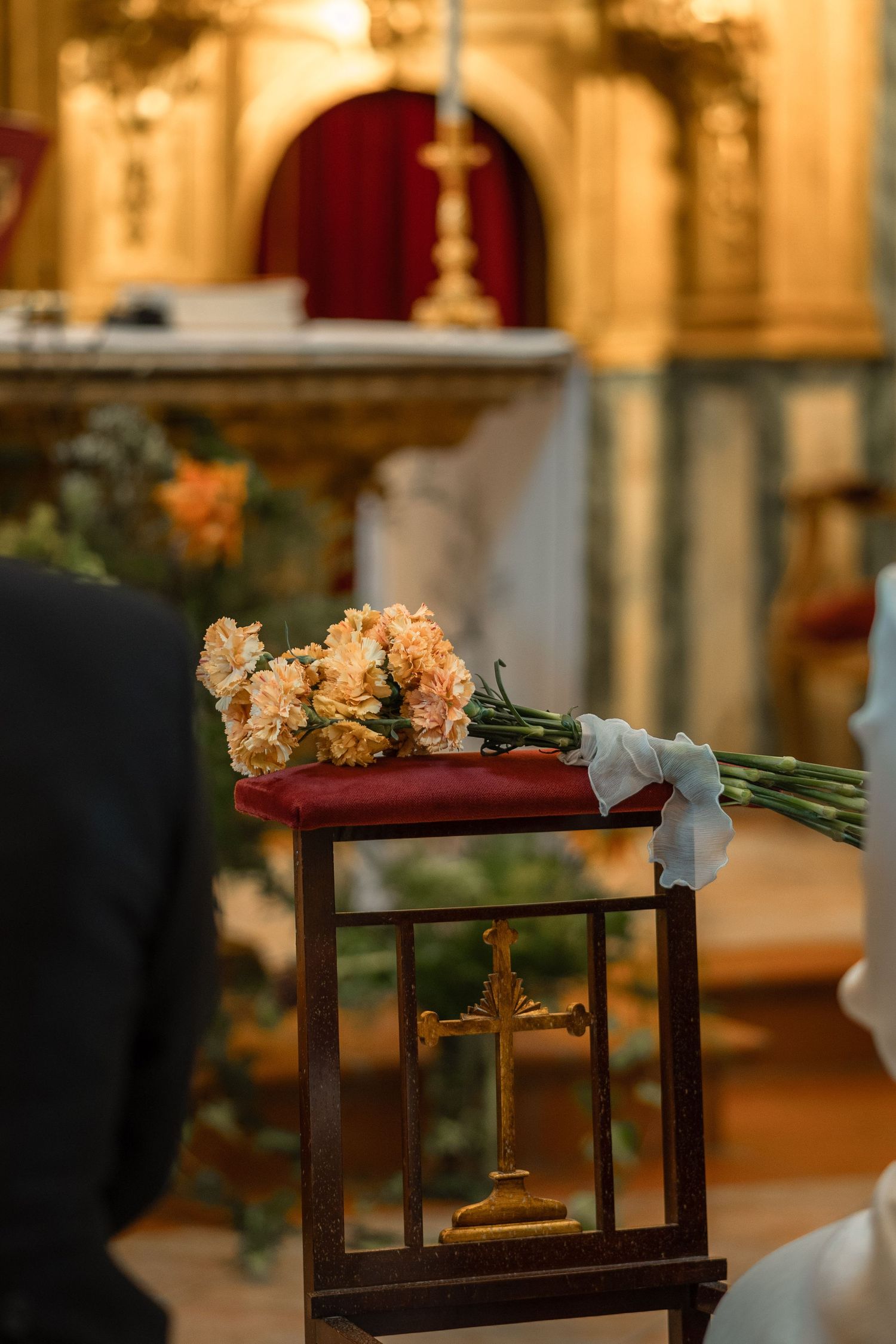 Peach floral bouquet resting on dark wooden church pews in warm lighting.