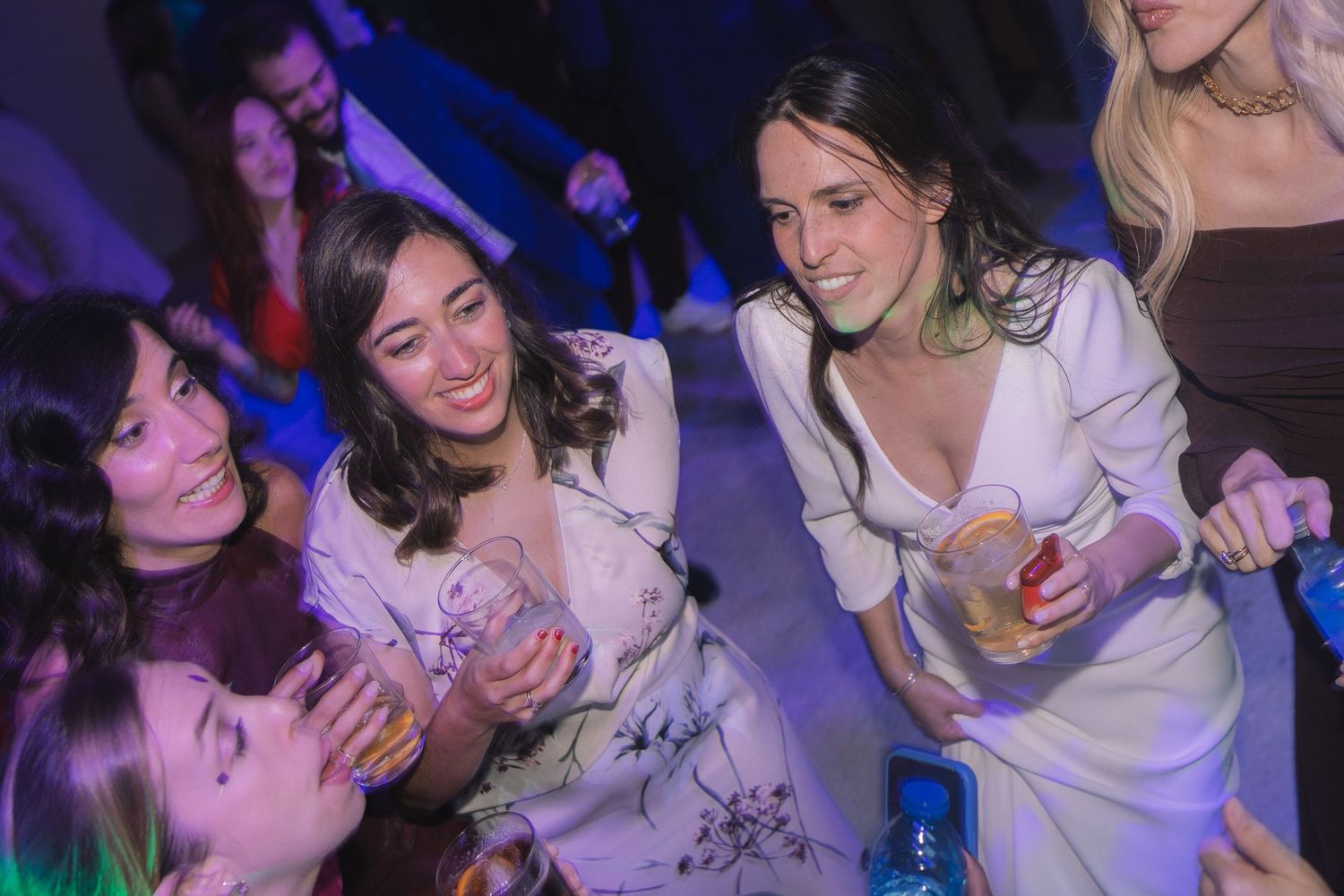 Wedding guests dance and celebrate together on a crowded dance floor with blue lighting effects.