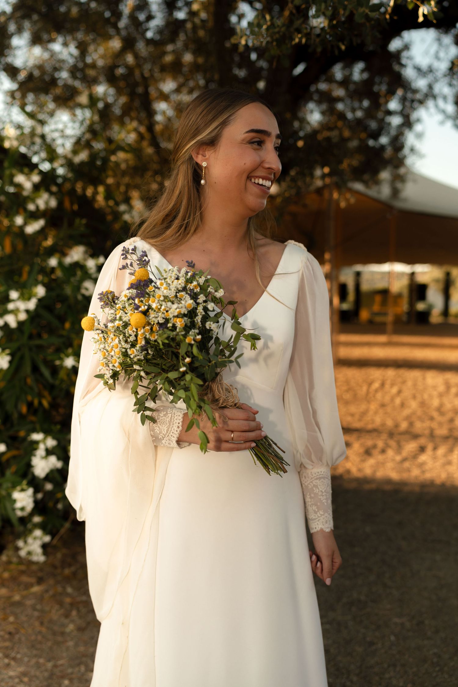 A bride in white holding a wildflower bouquet poses in golden sunset light.