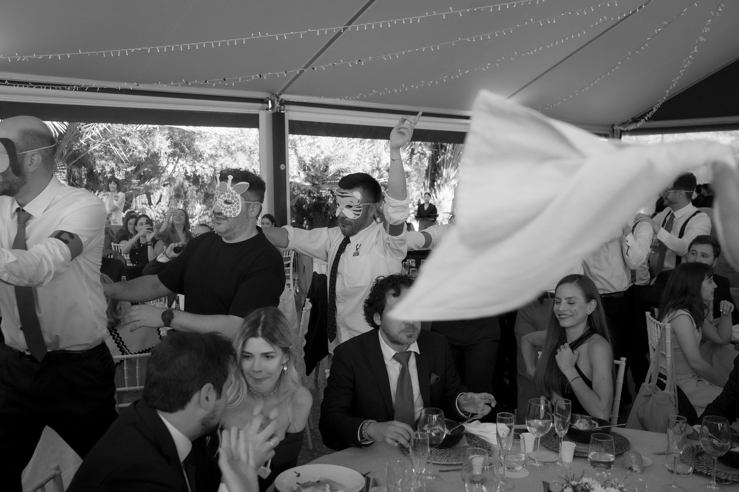 Wedding reception guests dance and celebrate under string lights at an outdoor venue.