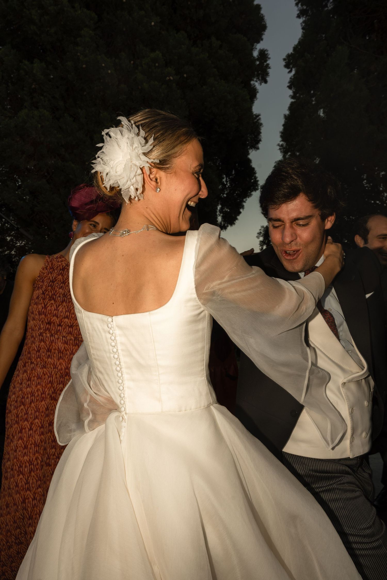 Dancing figures in white formal attire at an evening celebration.