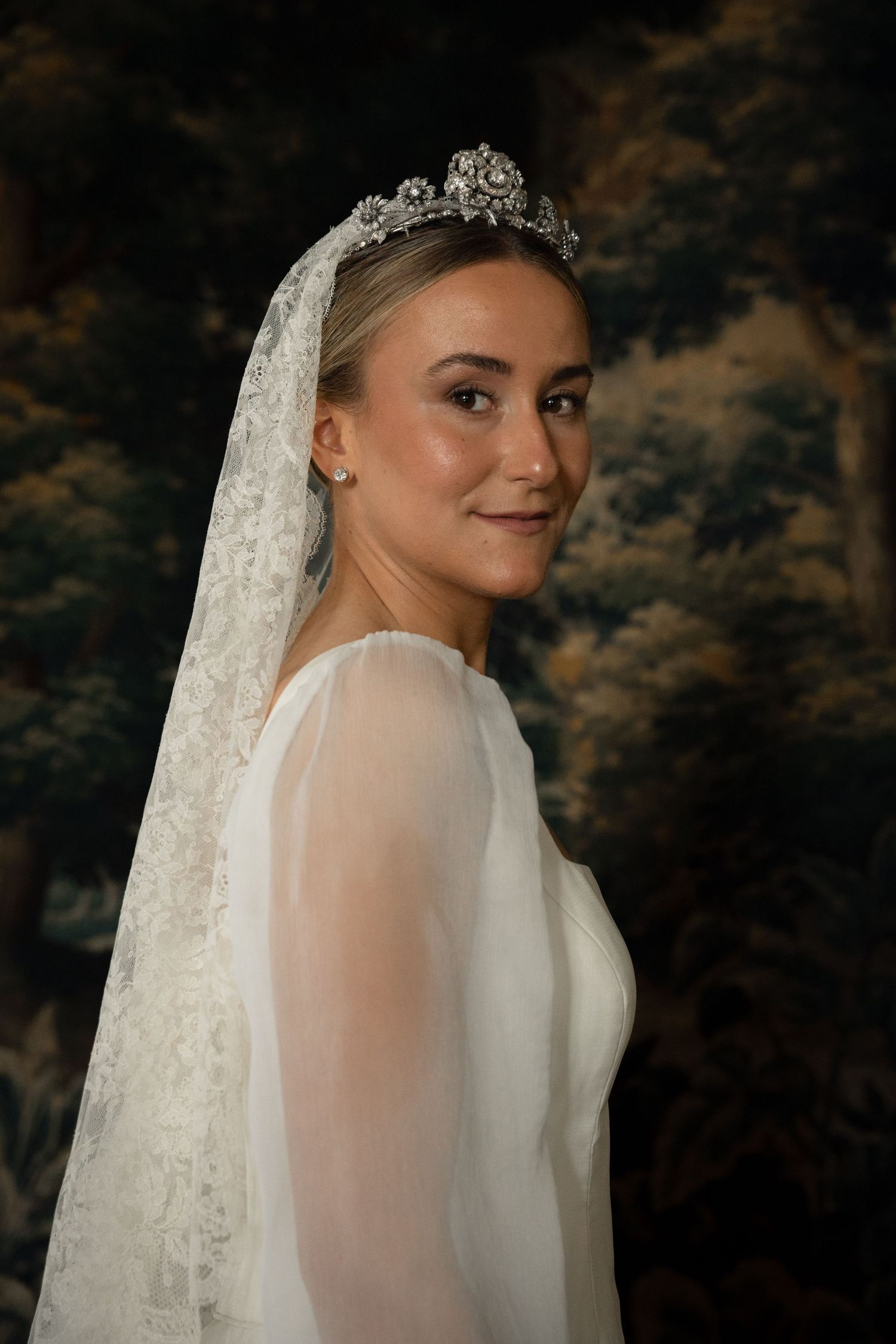 An elegant bridal portrait showcasing delicate lace veil and sparkling tiara against a dark background.