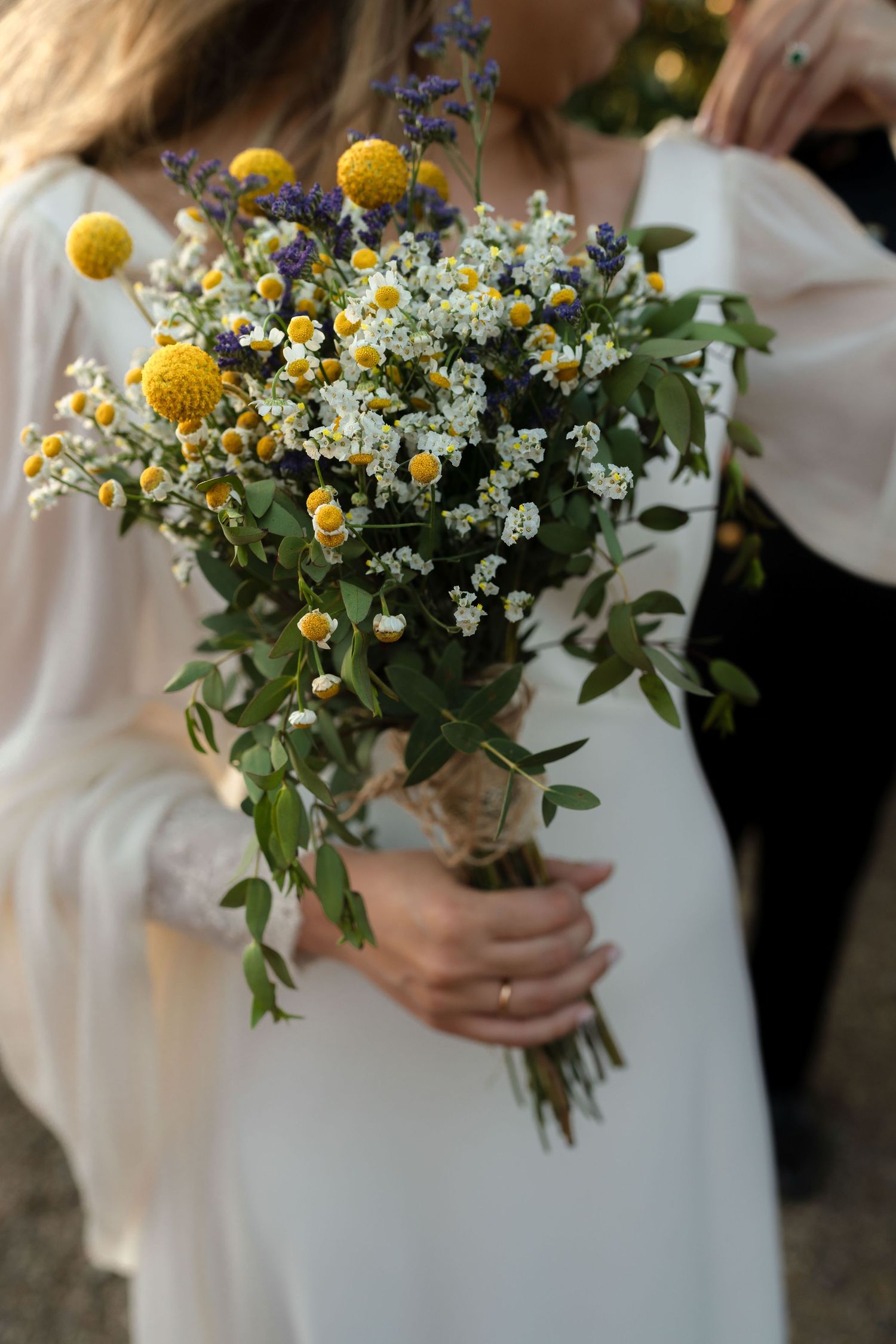 Detailed shots of a rustic wildflower bouquet with yellow and white flowers against a white dress.