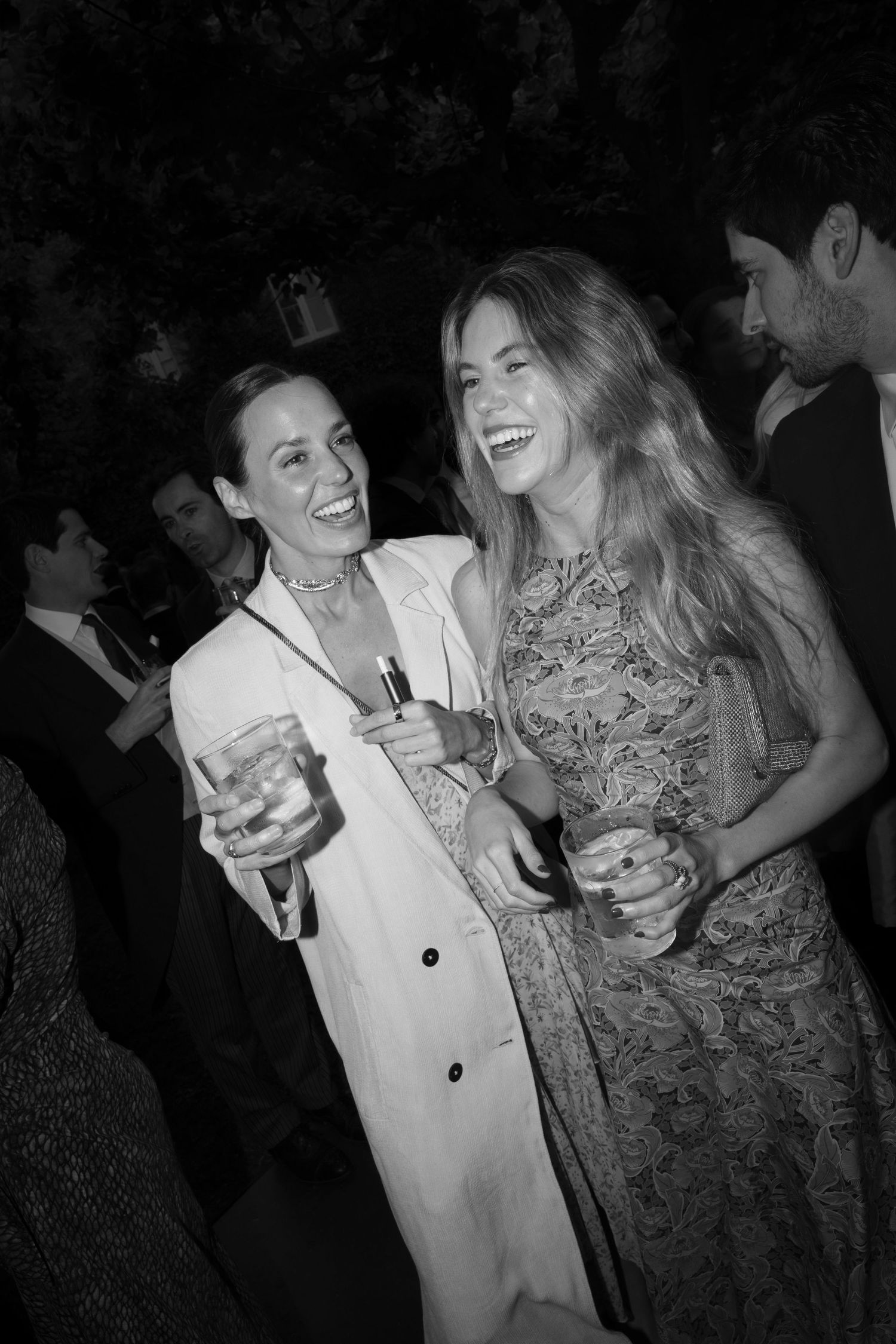Two people sharing drinks and laughter at a dimly lit party.