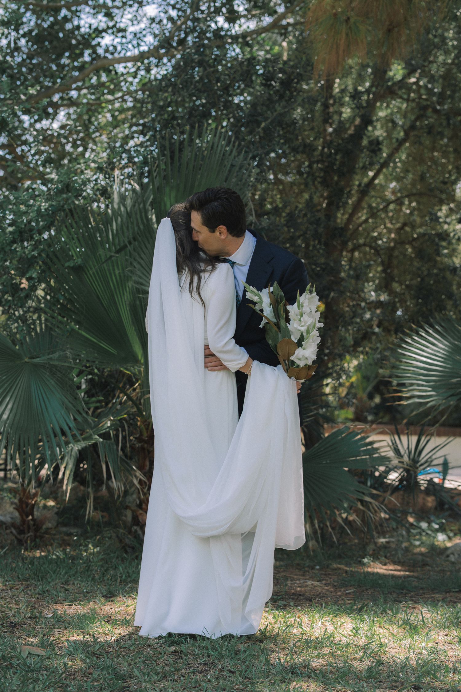 A romantic wedding photo session in a lush garden setting with palm trees and natural greenery.