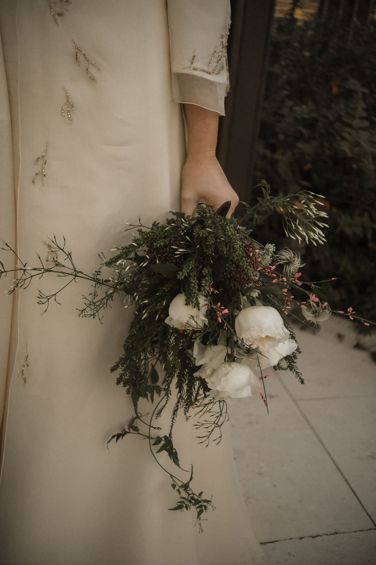 Wedding dress detail with delicate floral foliage bouquet against white fabric.