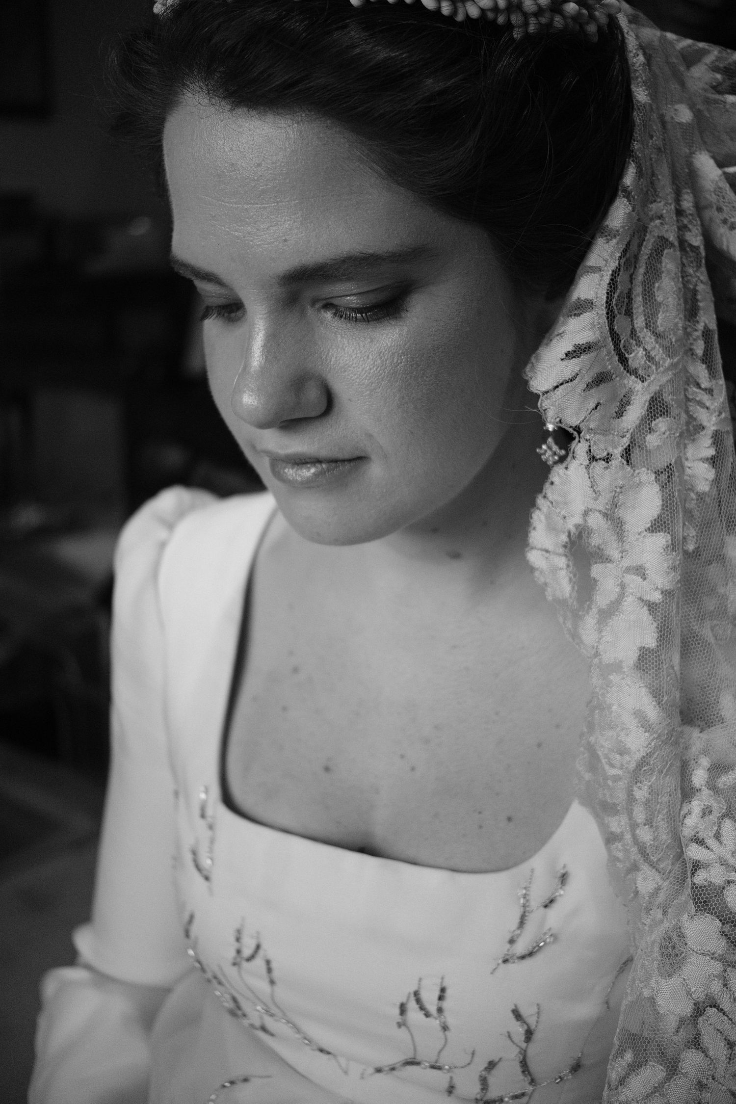 Close-up portrait of figure wearing lace veil and embroidered white dress in classic bridal style.