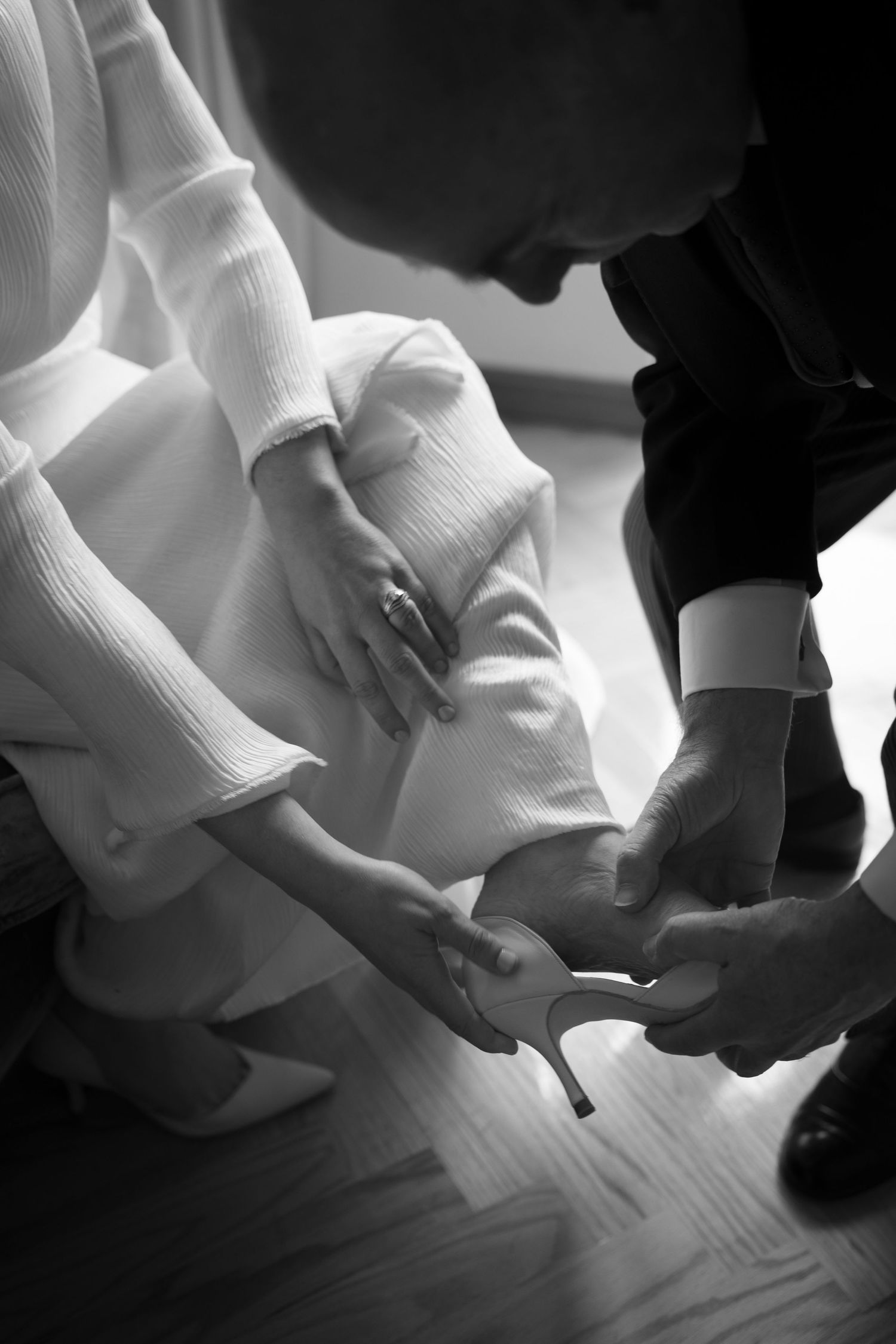 Black and white detail shot of hands adjusting wedding shoes.
