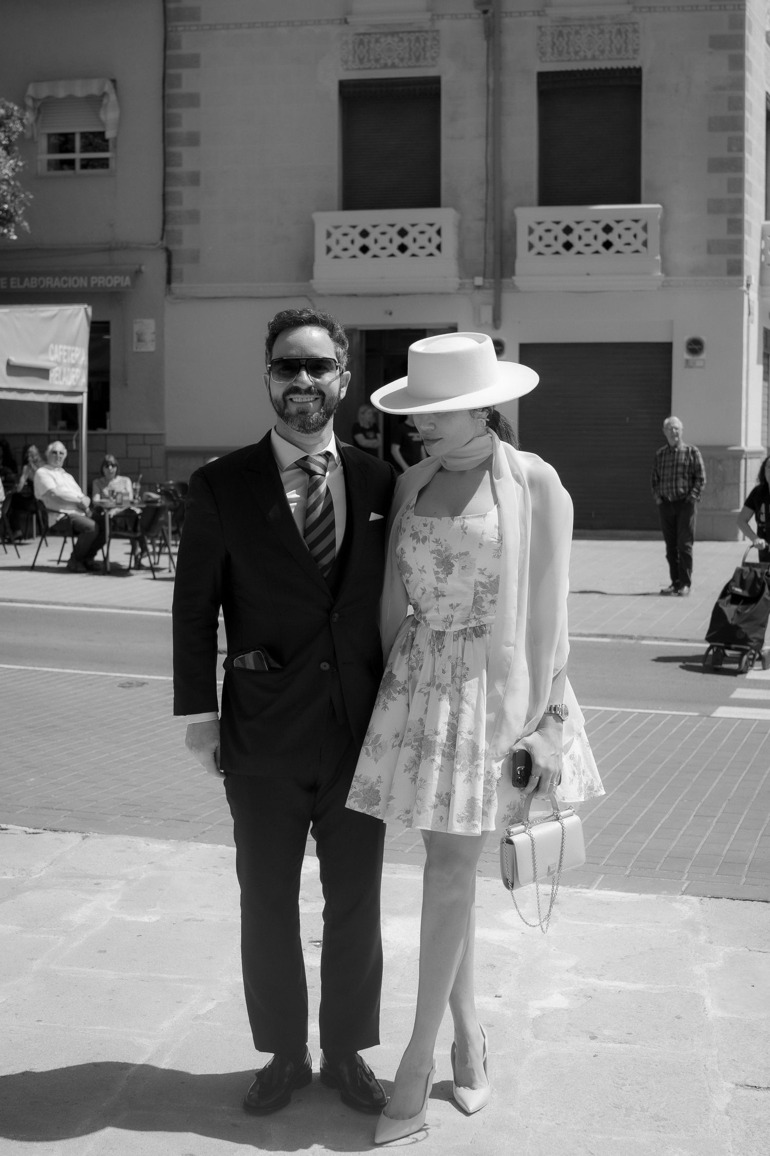 Couple in formal attire standing outside a building on a sunny day.