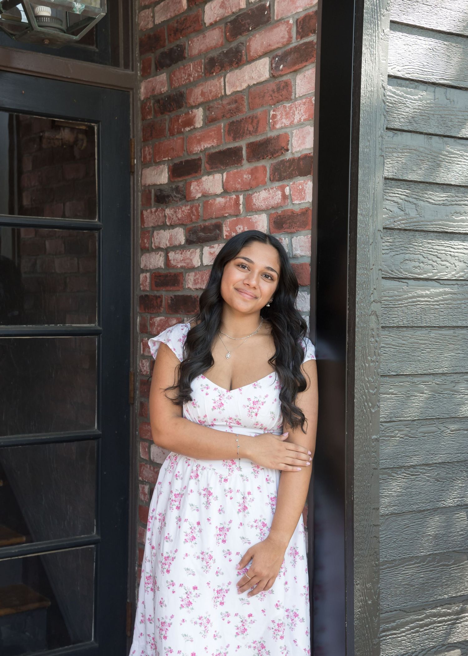 Person in floral dress poses against rustic brick wall with painted trim.
