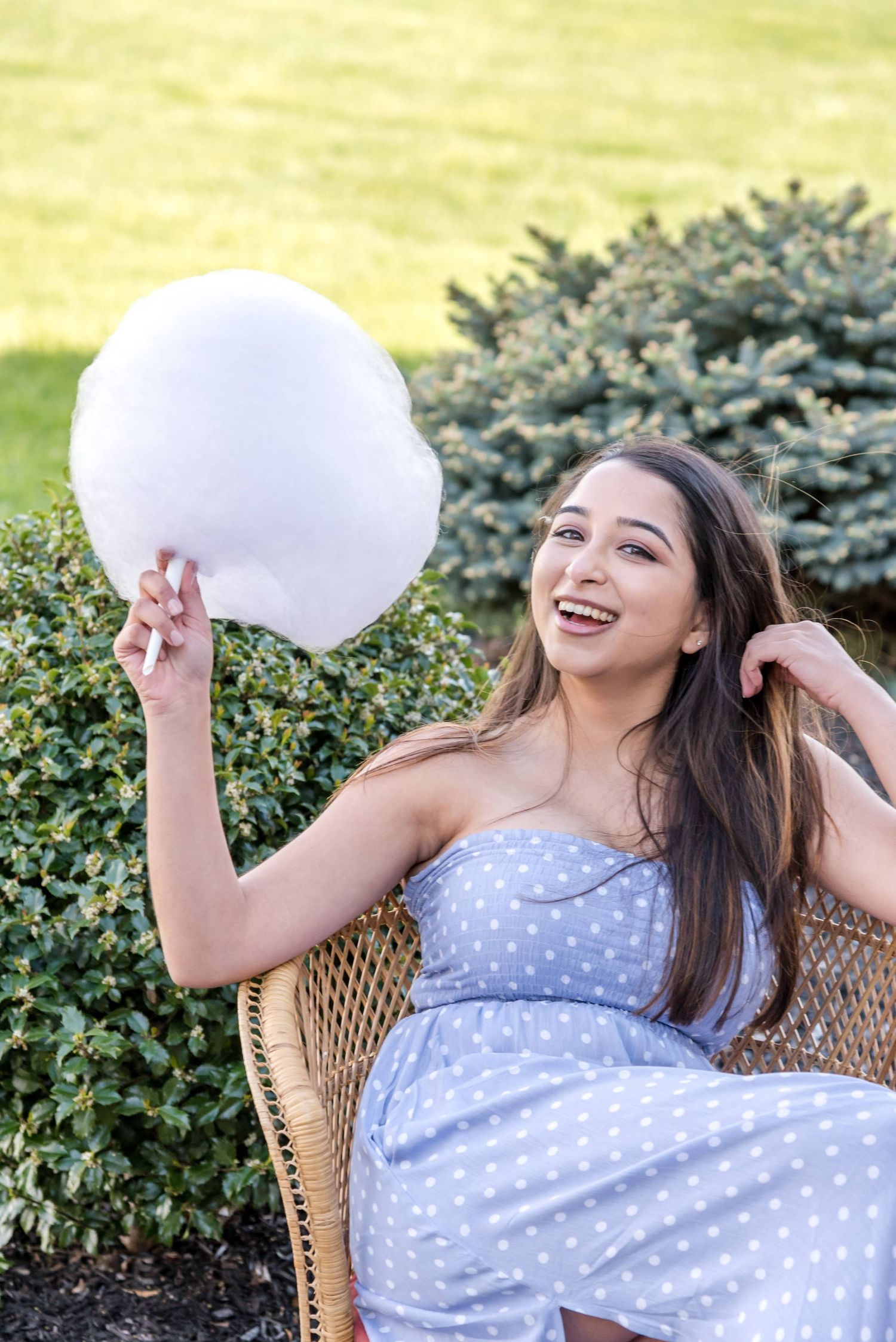 Woman in polka dot dress holding cotton candy while sitting in wicker chair outdoors.