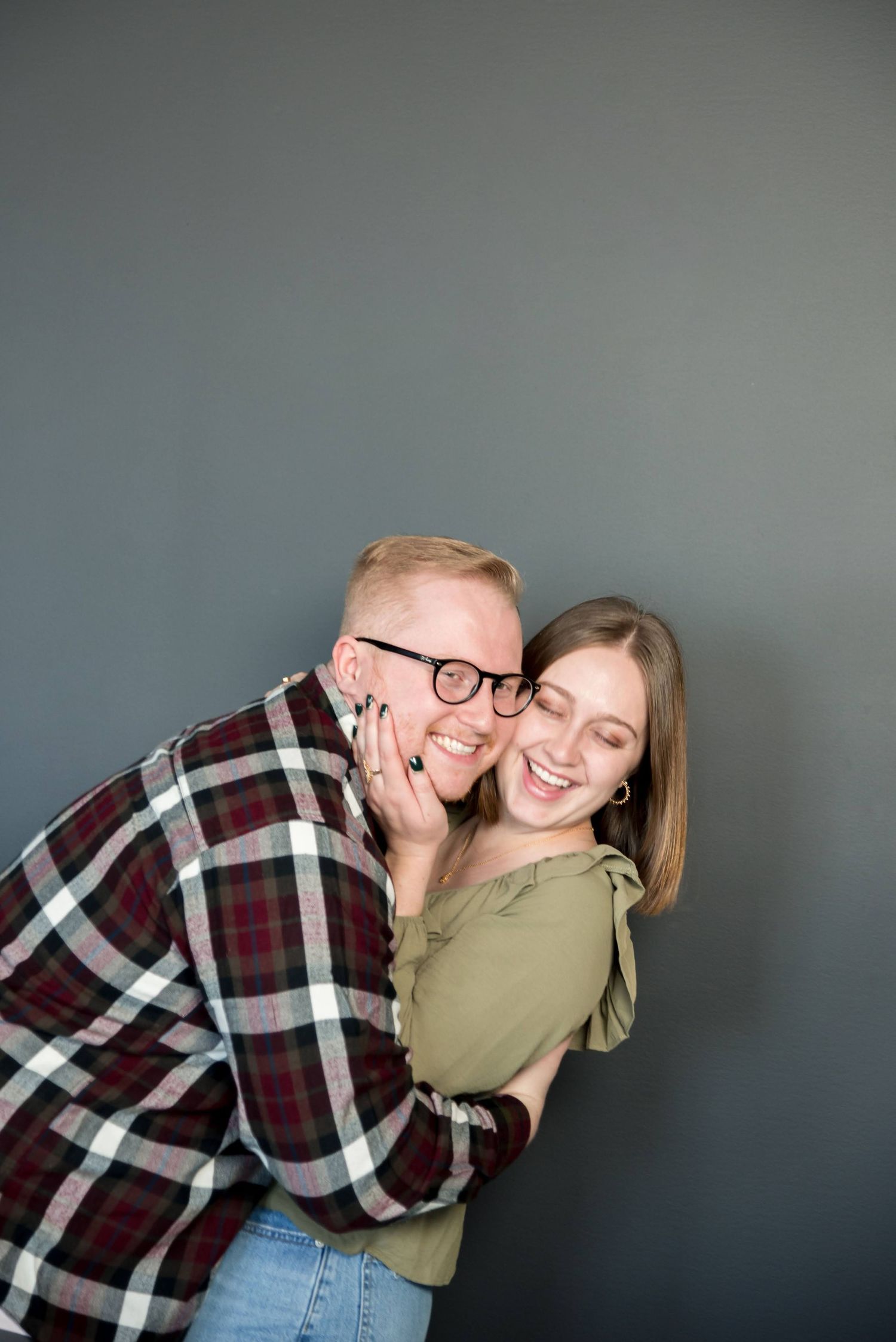 Joyful couple embracing and laughing against a grey background.