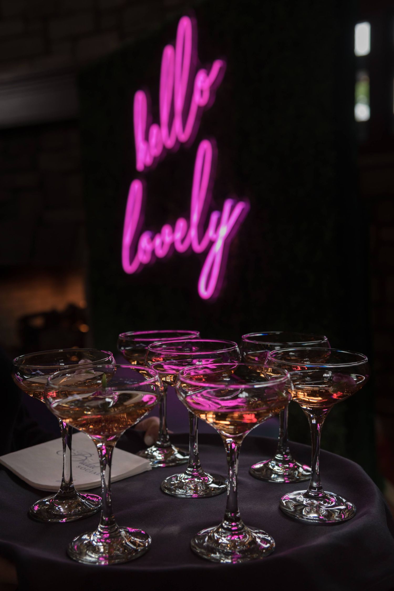 Elegant martini glasses arranged on dark table with pink neon lighting in background.