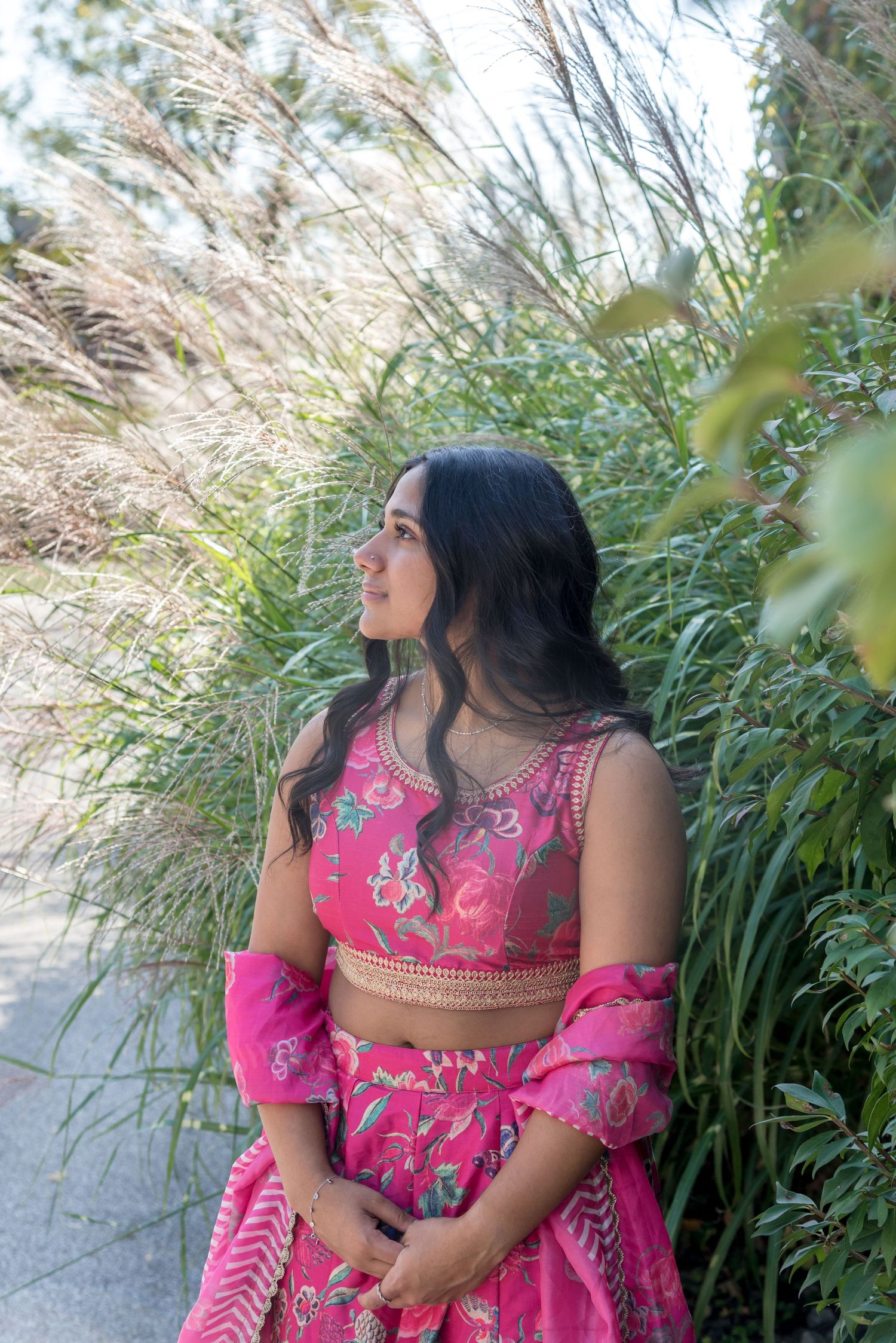 Portrait in a vibrant pink traditional dress among tall grass and natural scenery.