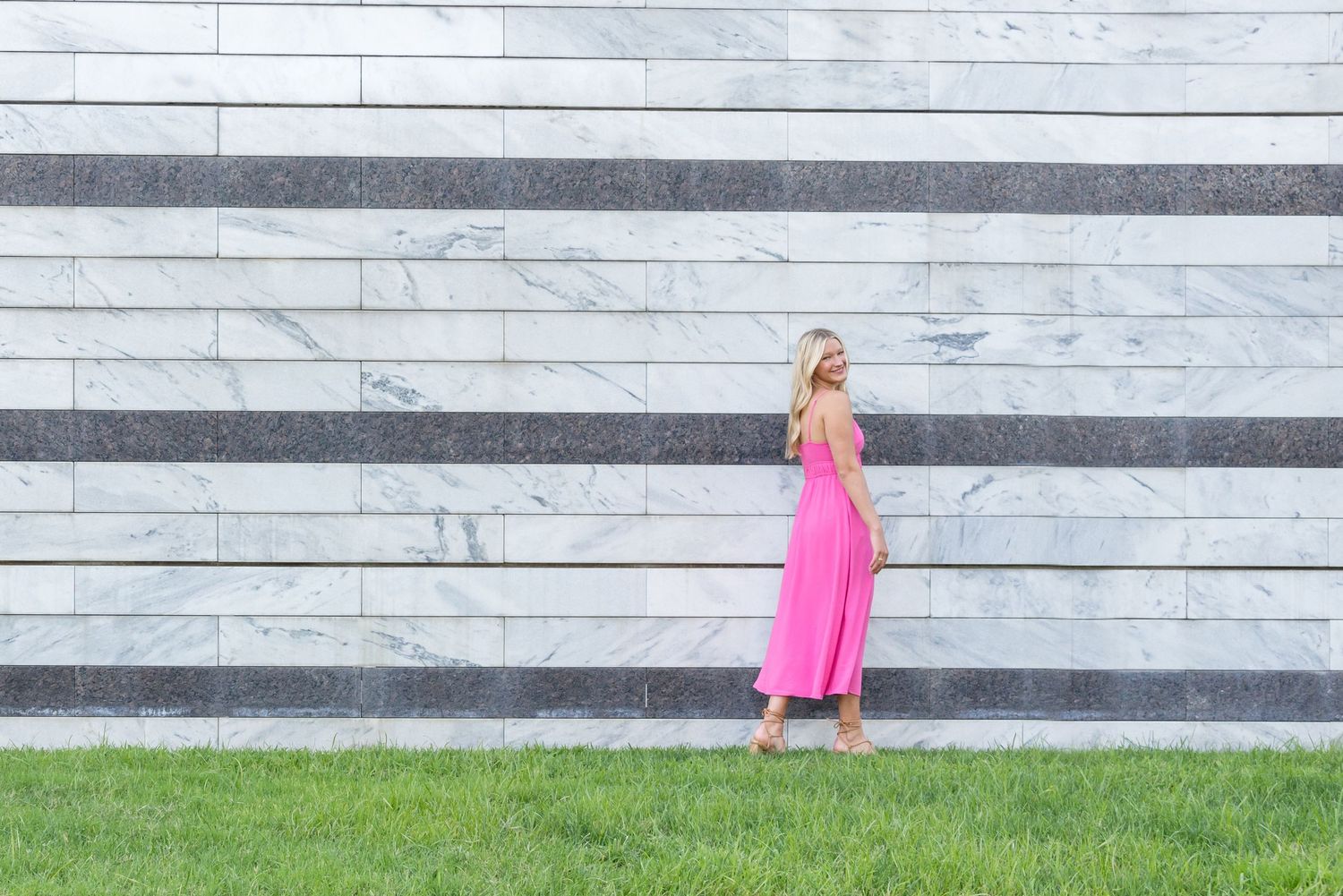 Pink dress against white and gray striped wall with grass in foreground.