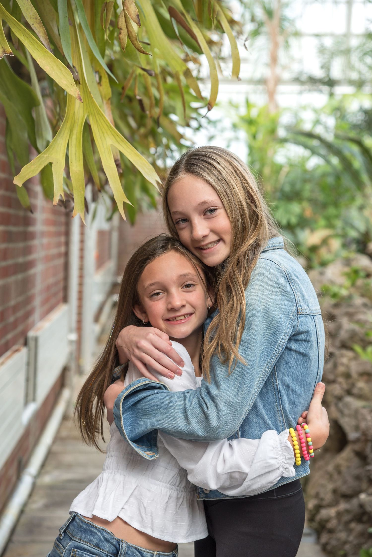 Two children sharing playful hugs and laughter under leafy green foliage.