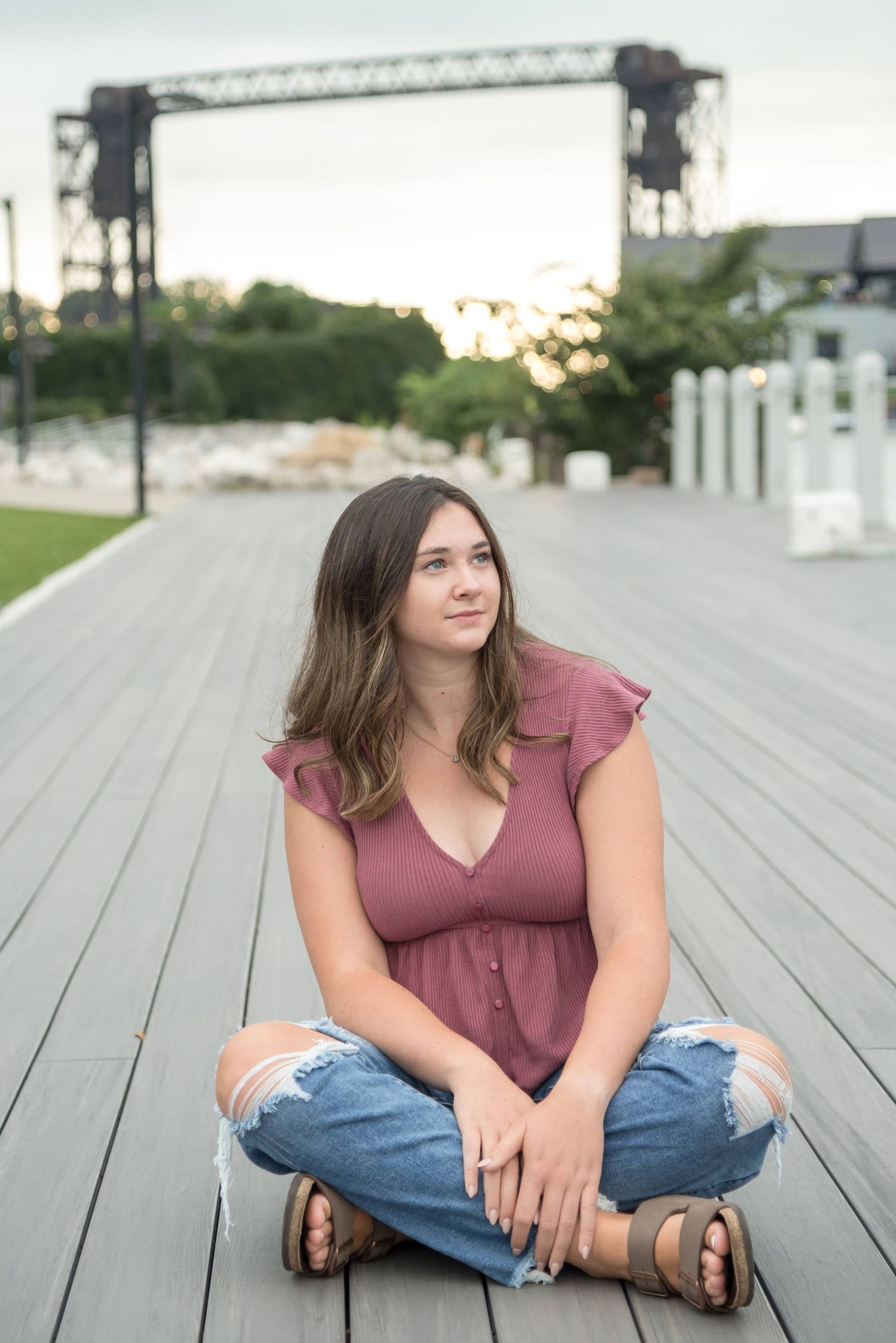 Person in mauve top and jeans sitting on wooden deck during sunset.