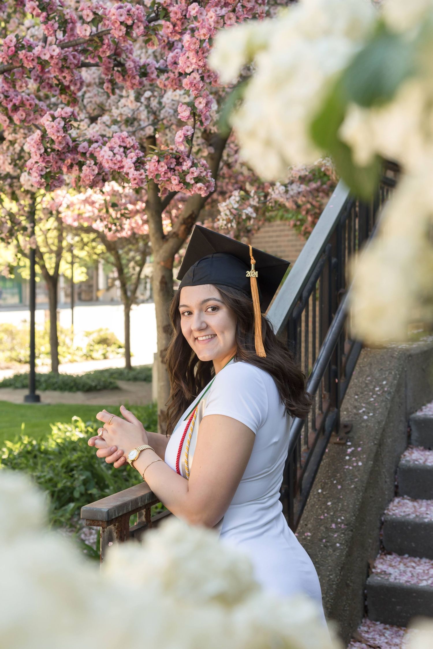 Graduate poses under blooming cherry blossom trees in springtime.