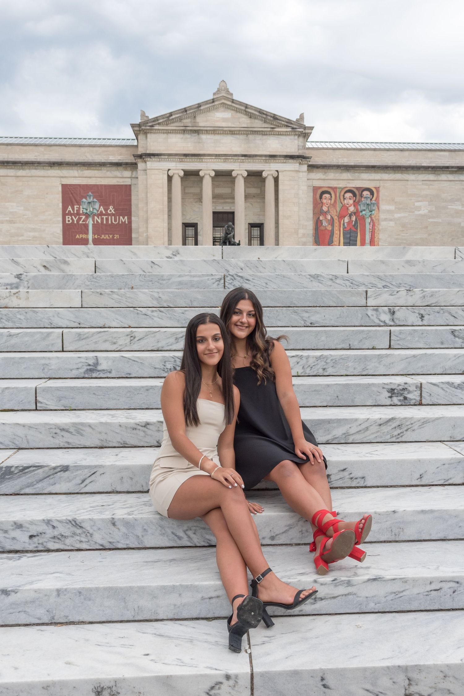 Two friends sitting on marble steps outside a classical museum building.
