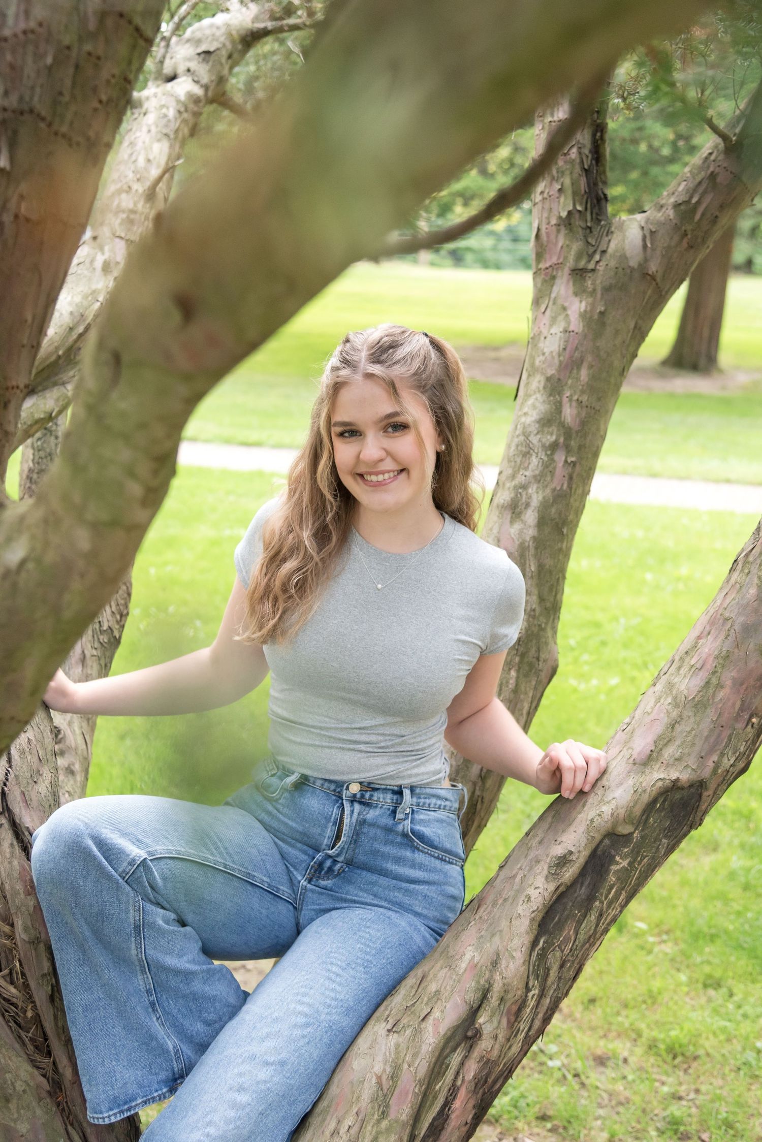 Person in casual attire poses among tree branches in park setting.