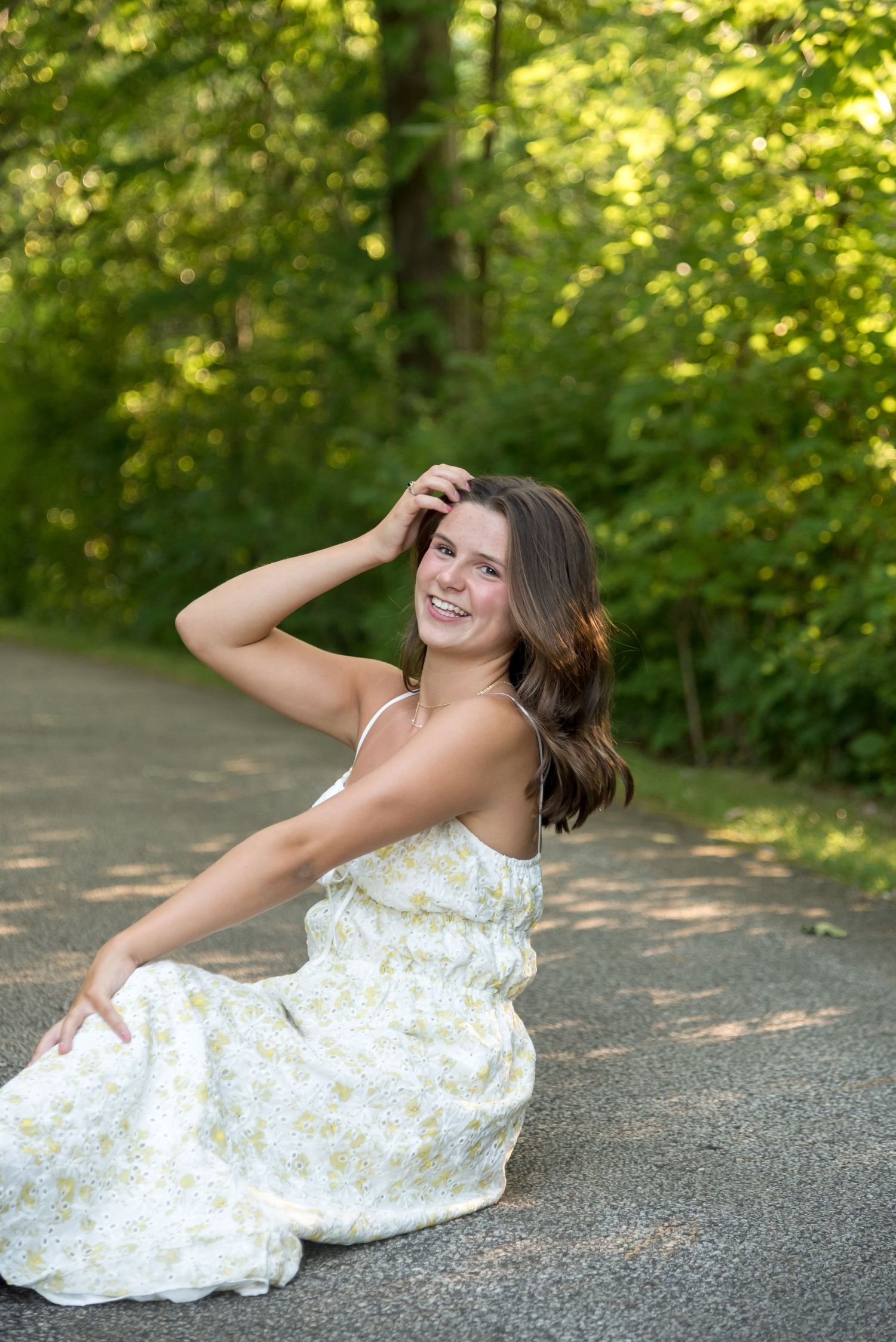 Person in floral dress sits gracefully on a sunlit forest path.