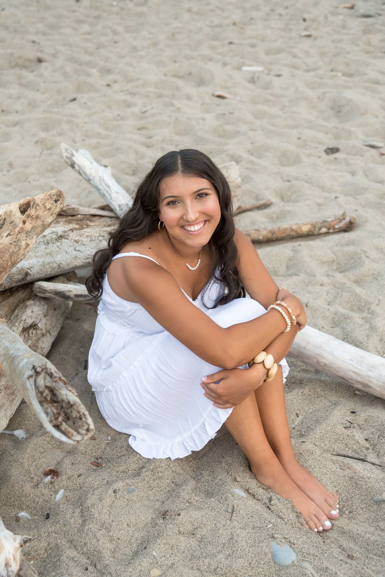 Person in white dress reclining on beach sand next to driftwood.