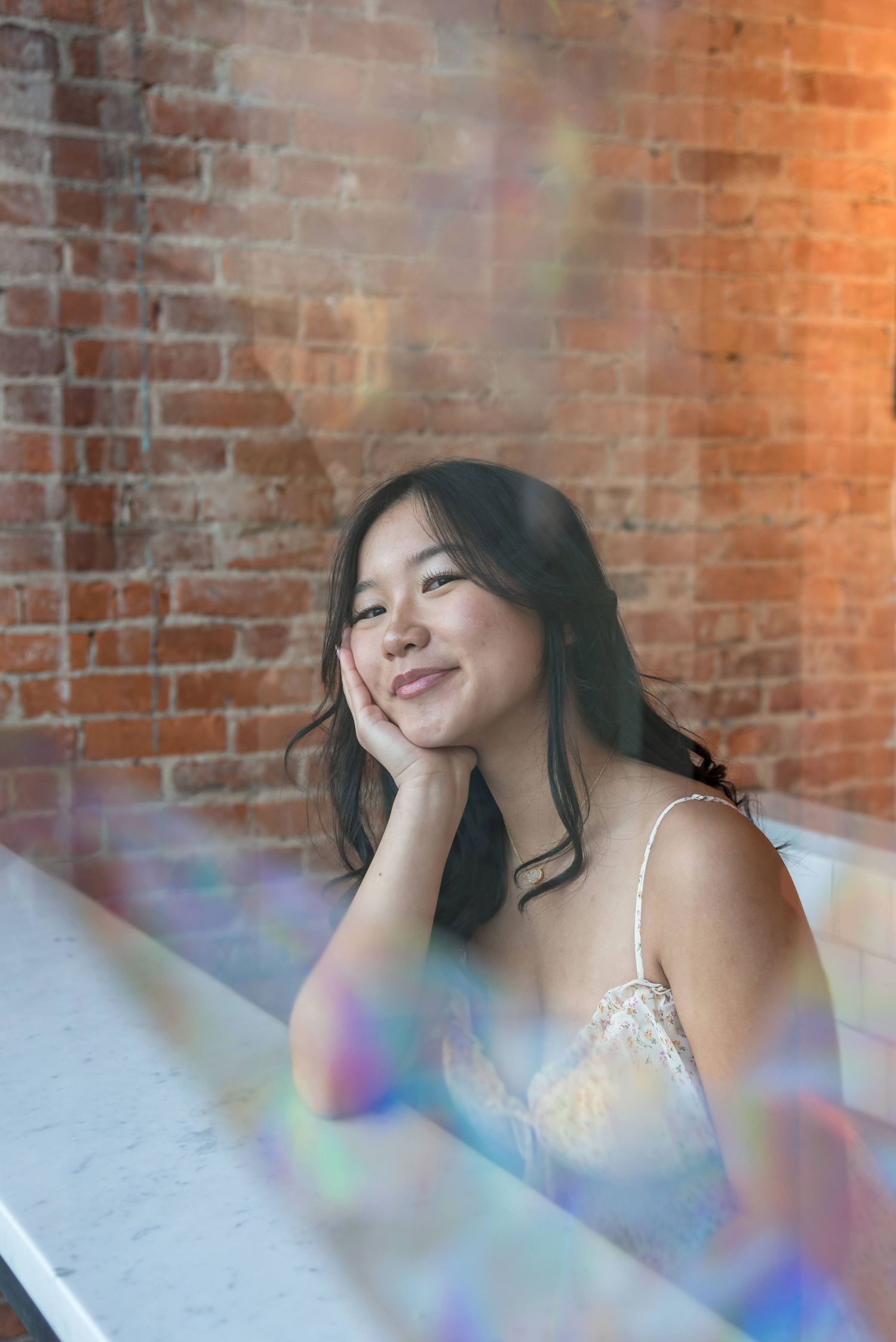 Portrait against brick wall with rainbow light prism effects.