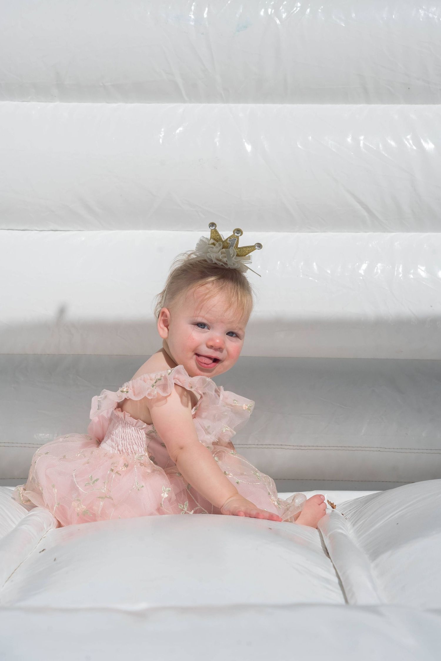 Baby wearing pink dress and tiny crown during professional photoshoot.