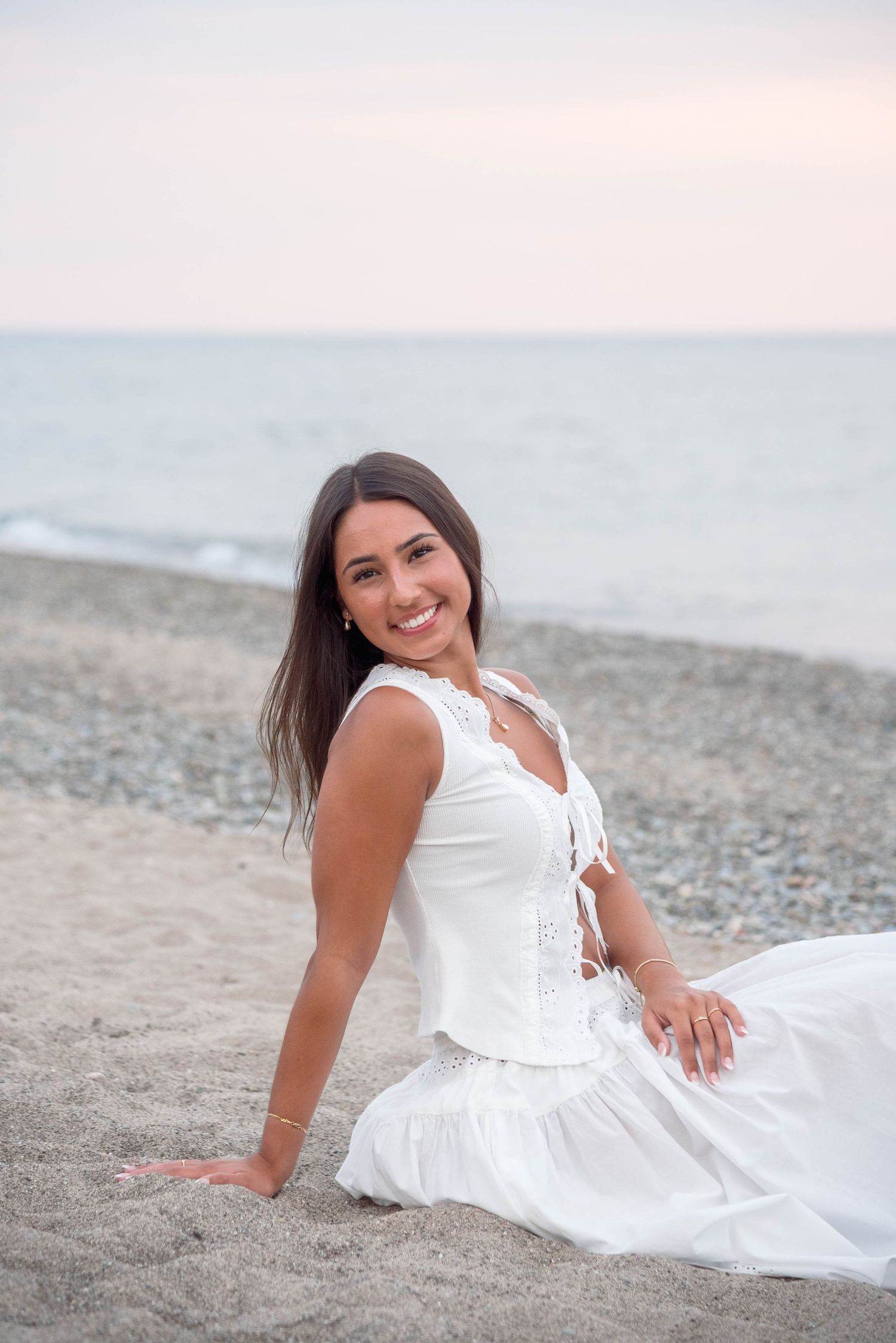 Woman in white dress poses gracefully on a beach at sunset.