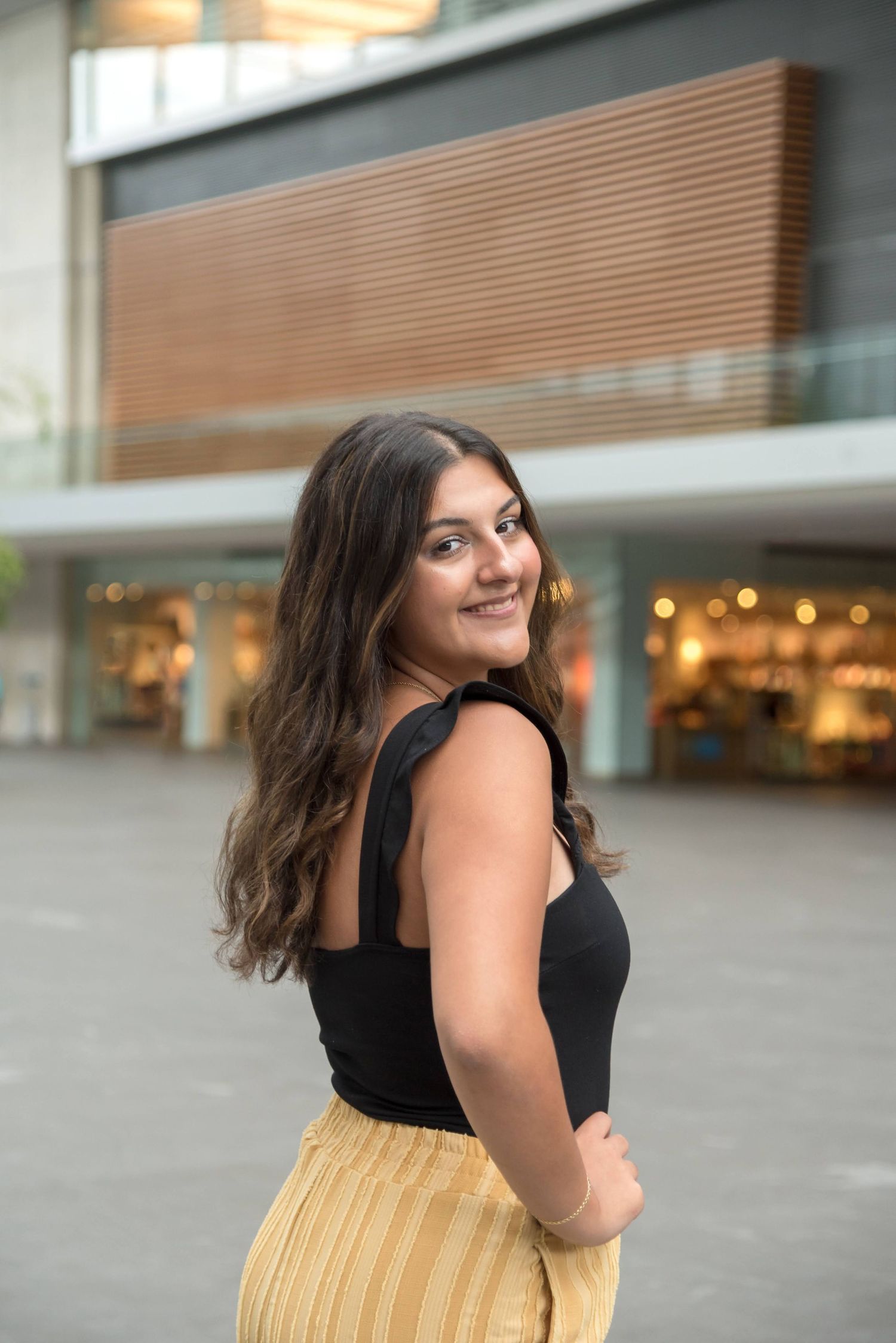 Person in black top and yellow skirt poses outside modern building with glass windows.