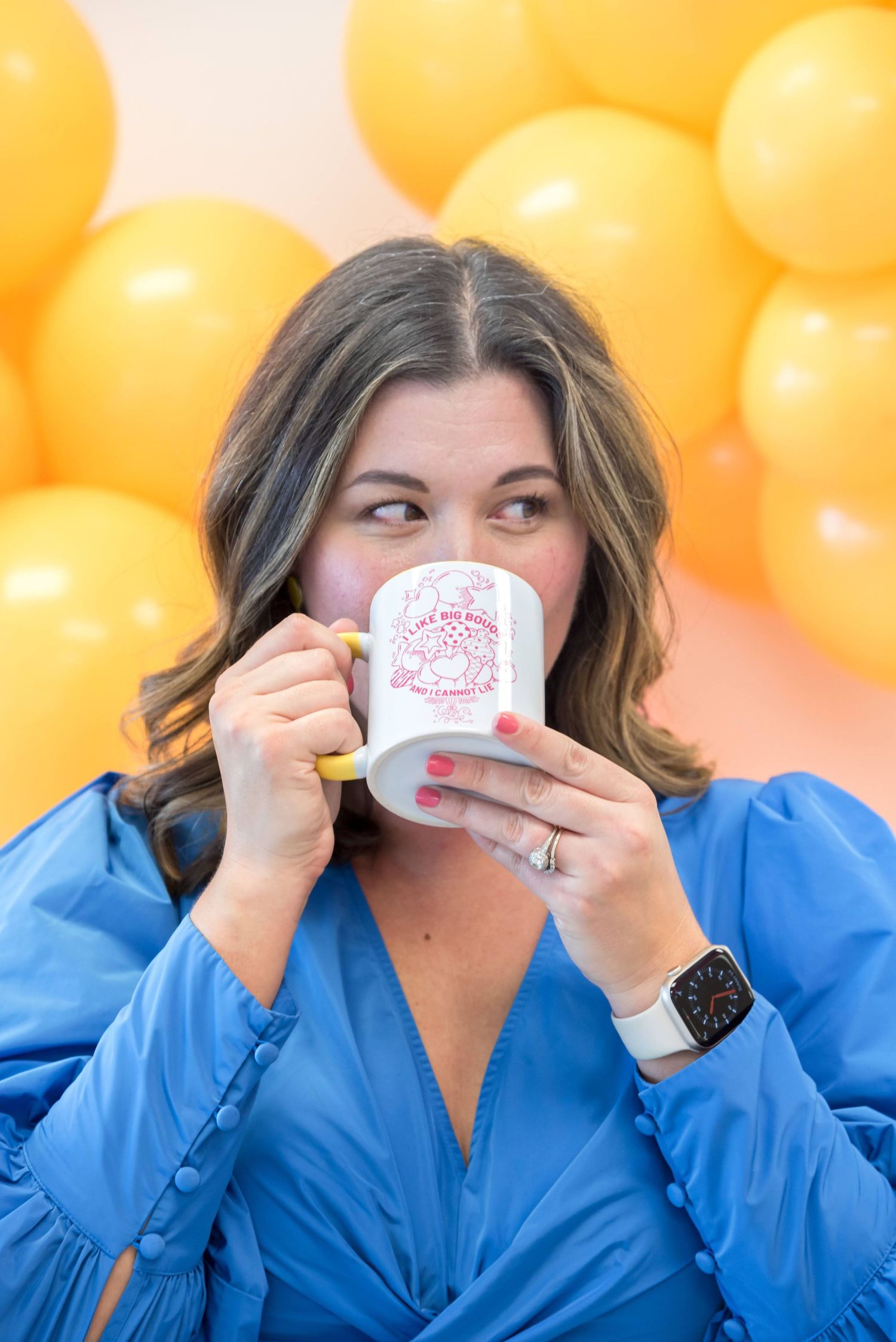 Someone in blue robe drinking from teacup against orange balloon background.