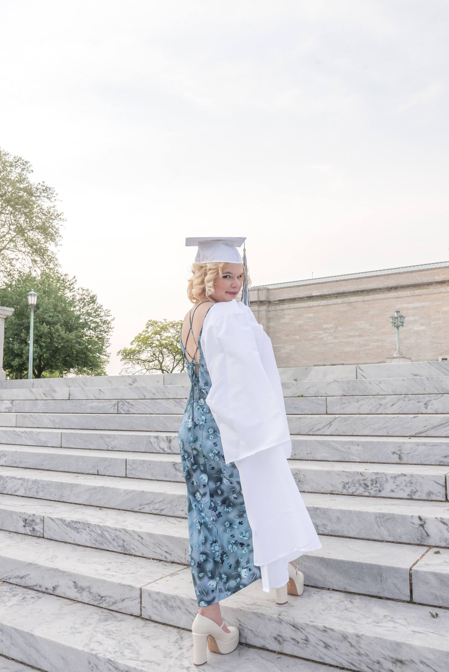 Person in graduation attire walking up marble steps outdoors.