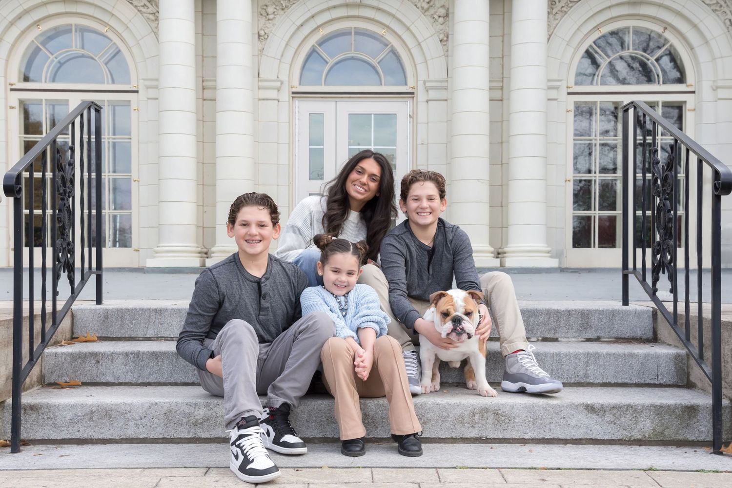 Family and pet dog posing together on white stone steps of classical building.