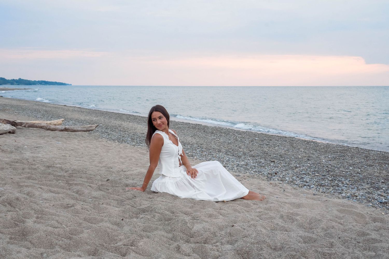 A white dress photoshoot on a beach at sunset with calm waters in the background.