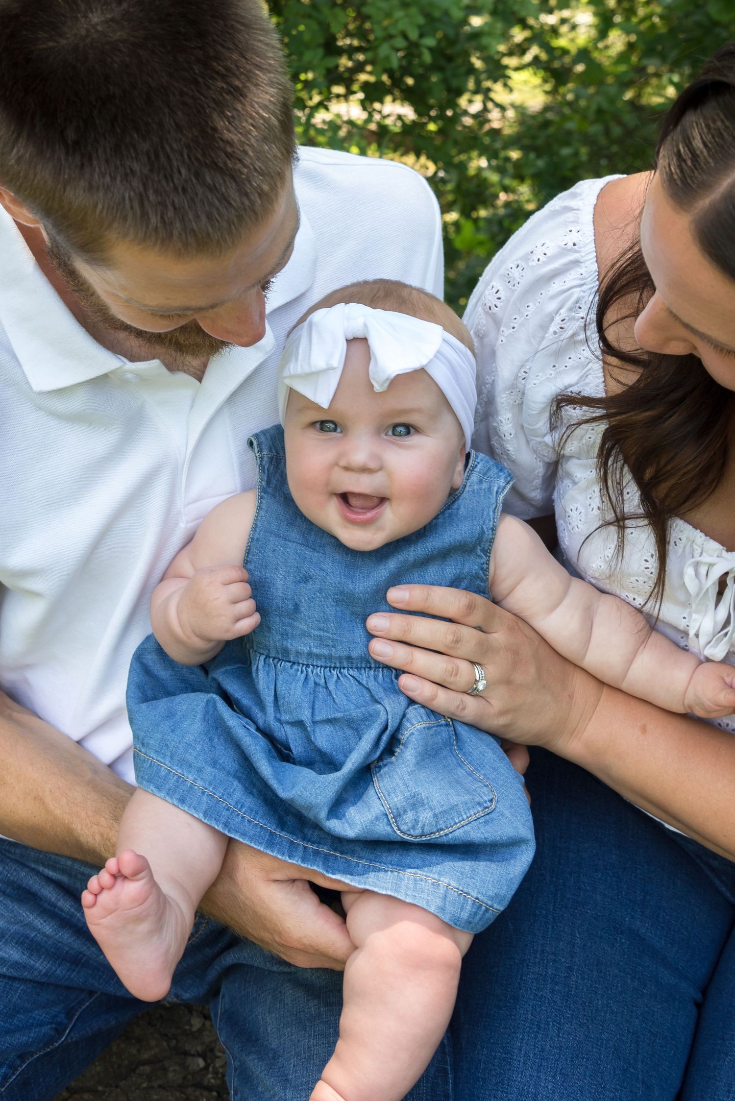 Family shares playful moments with baby wearing denim outfit outdoors.