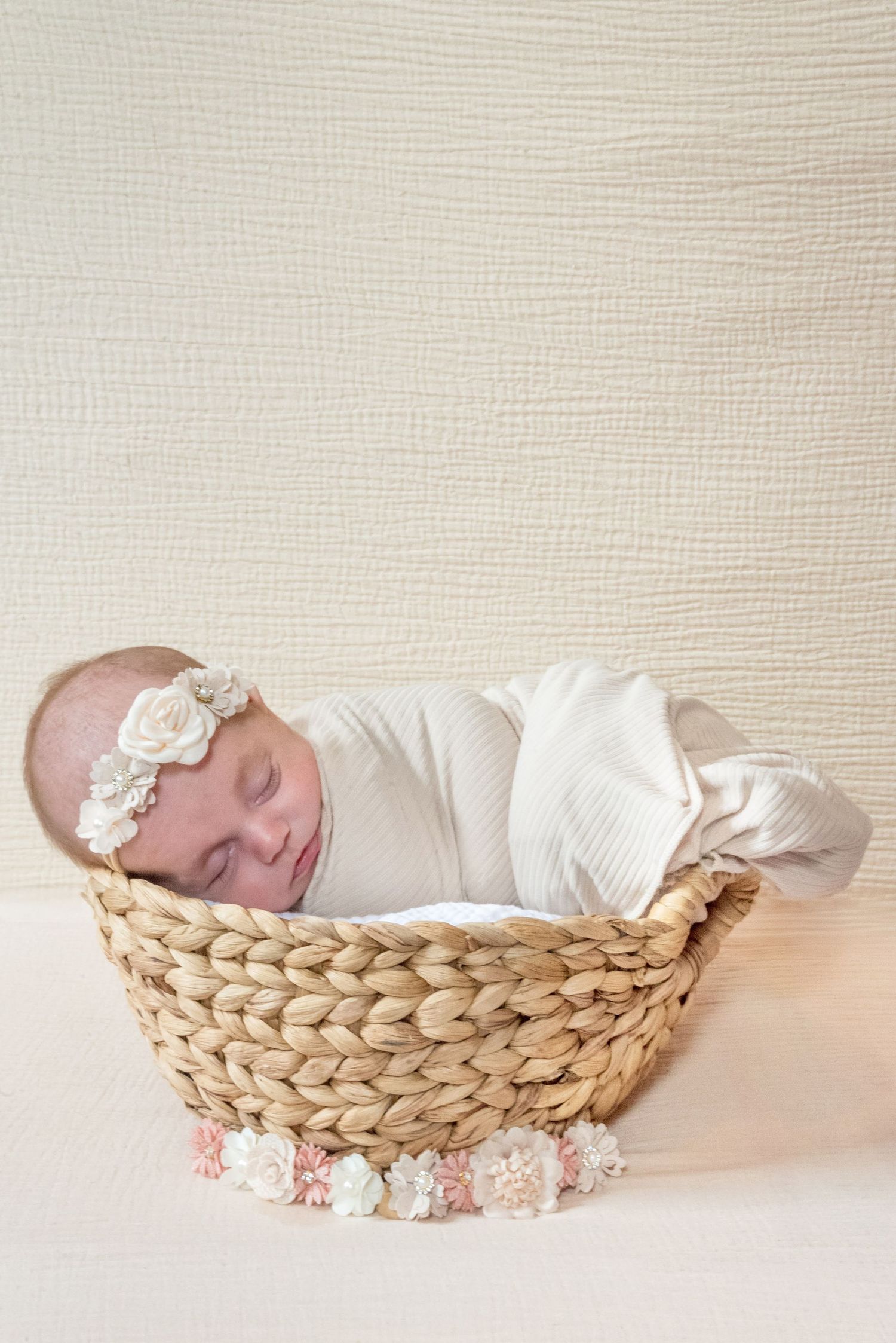 A sleeping newborn in white swaddle lying peacefully in a woven basket.
