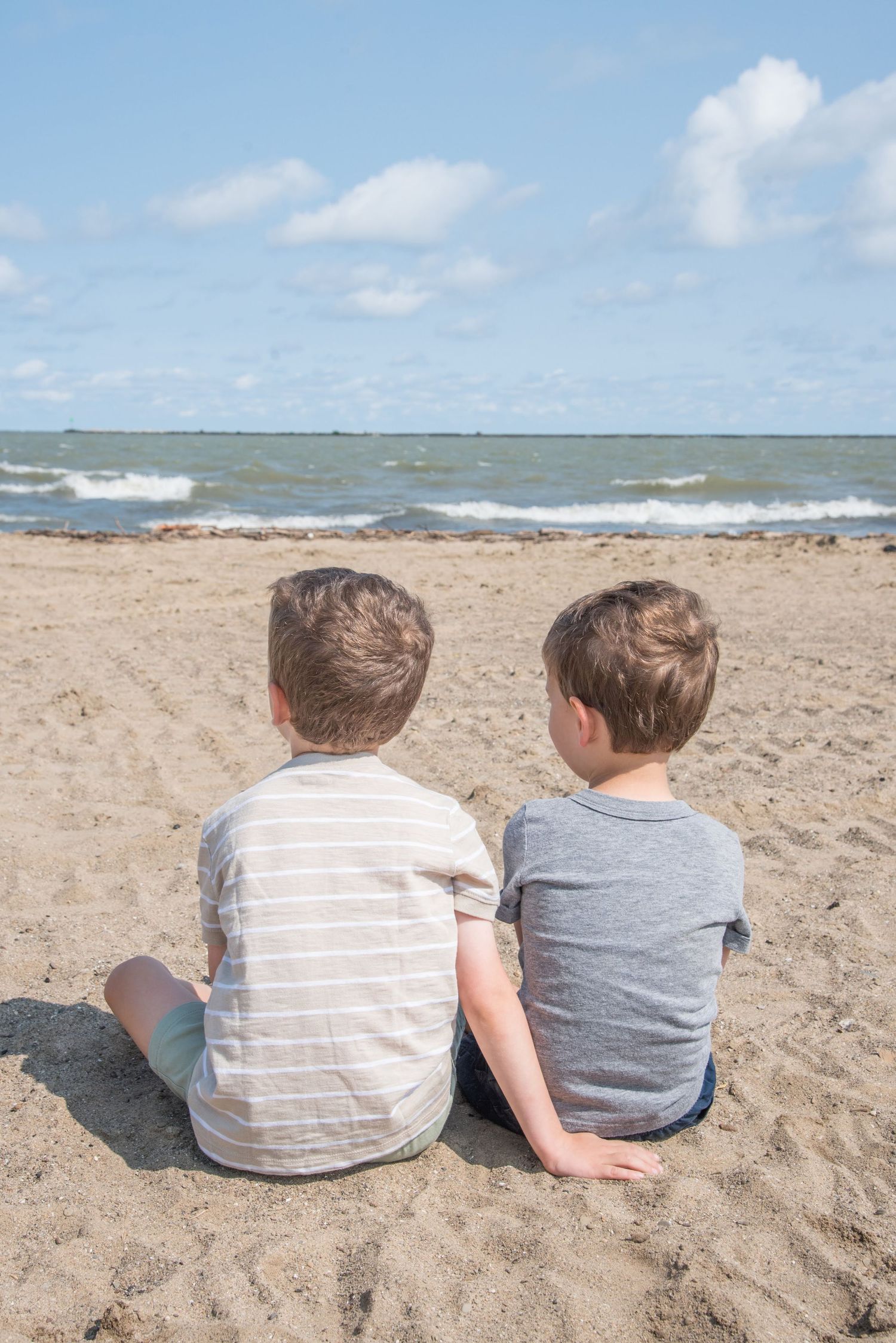 Two children sitting side by side on beach watching the ocean horizon.