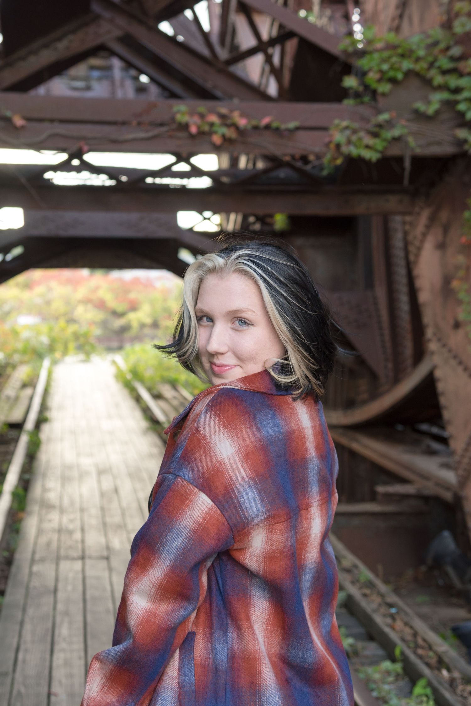Person wrapped in a red and blue plaid blanket sitting on wooden planks.