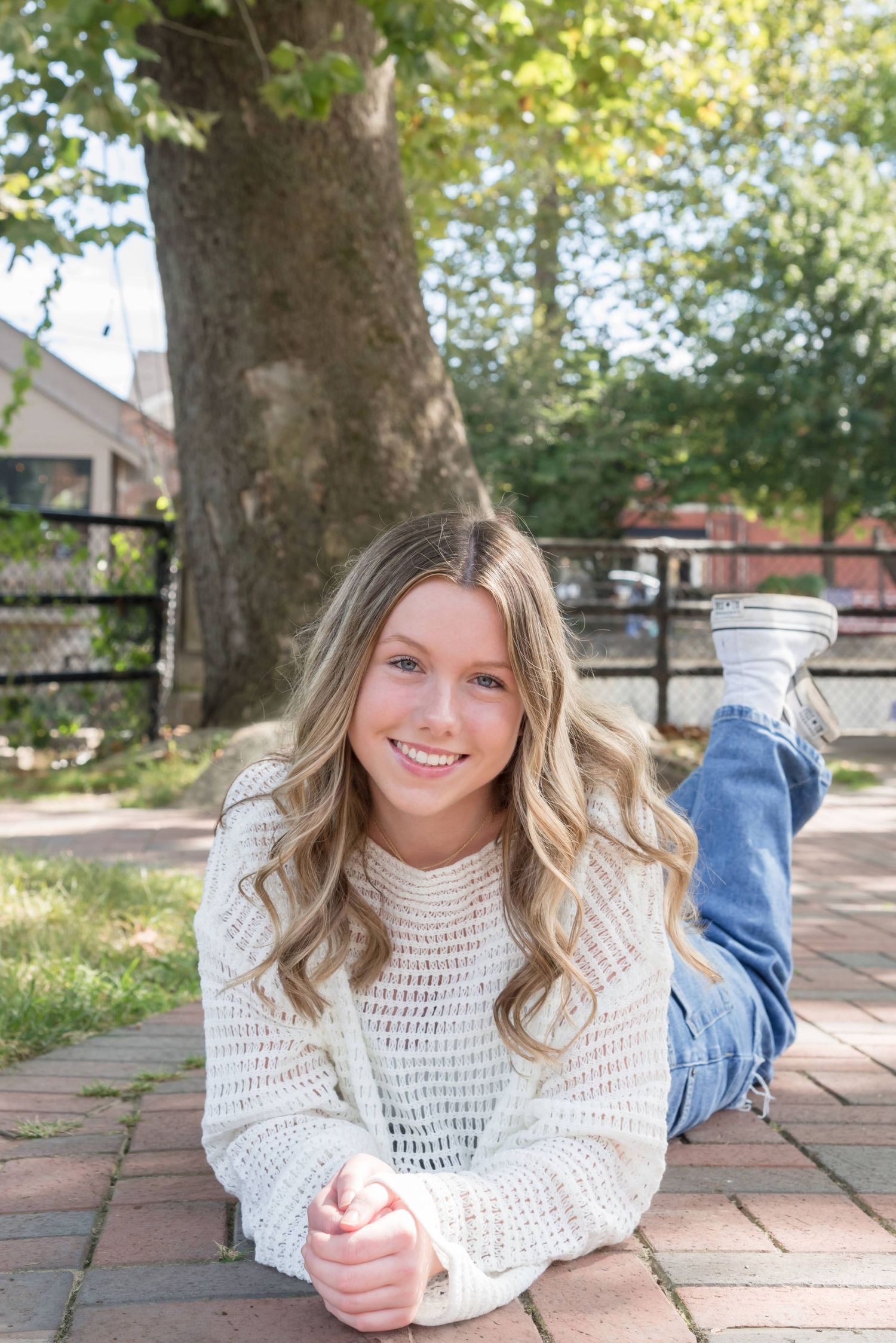 Person in knit sweater lies on brick patio under tree canopy.