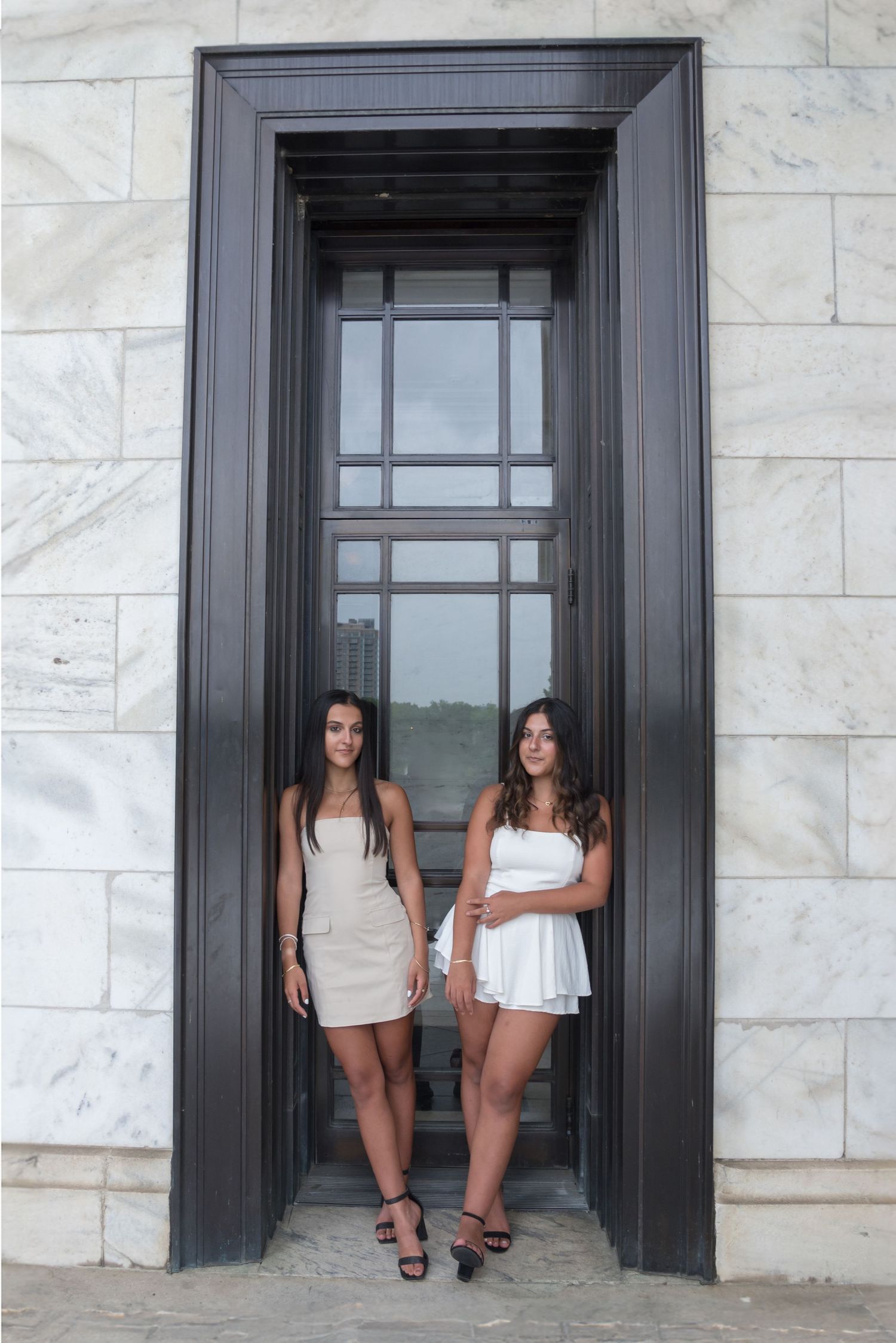Two people pose in a large black-framed doorway of a marble building.