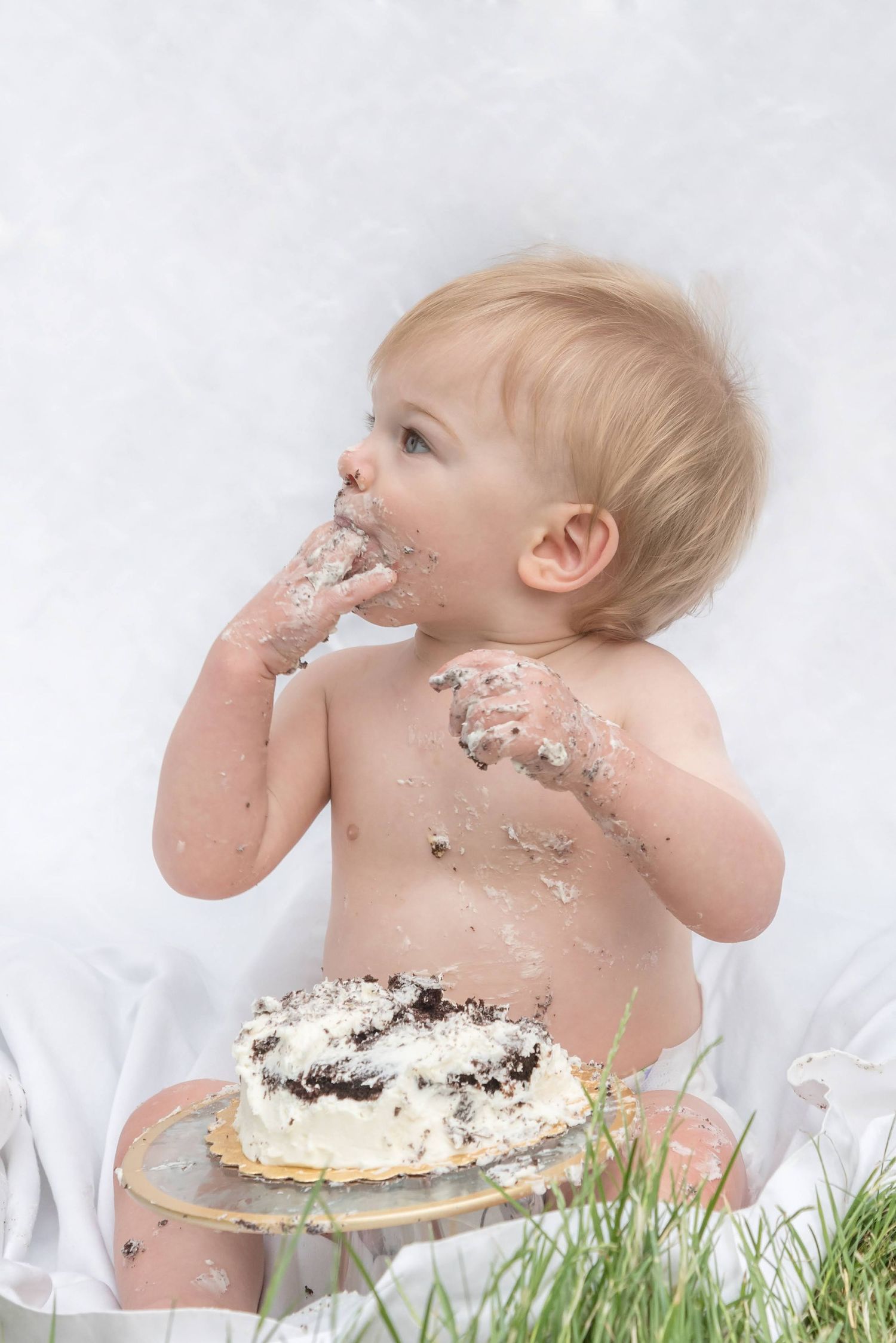 Baby enjoying a messy cake smash photo session with white frosting and decorations.