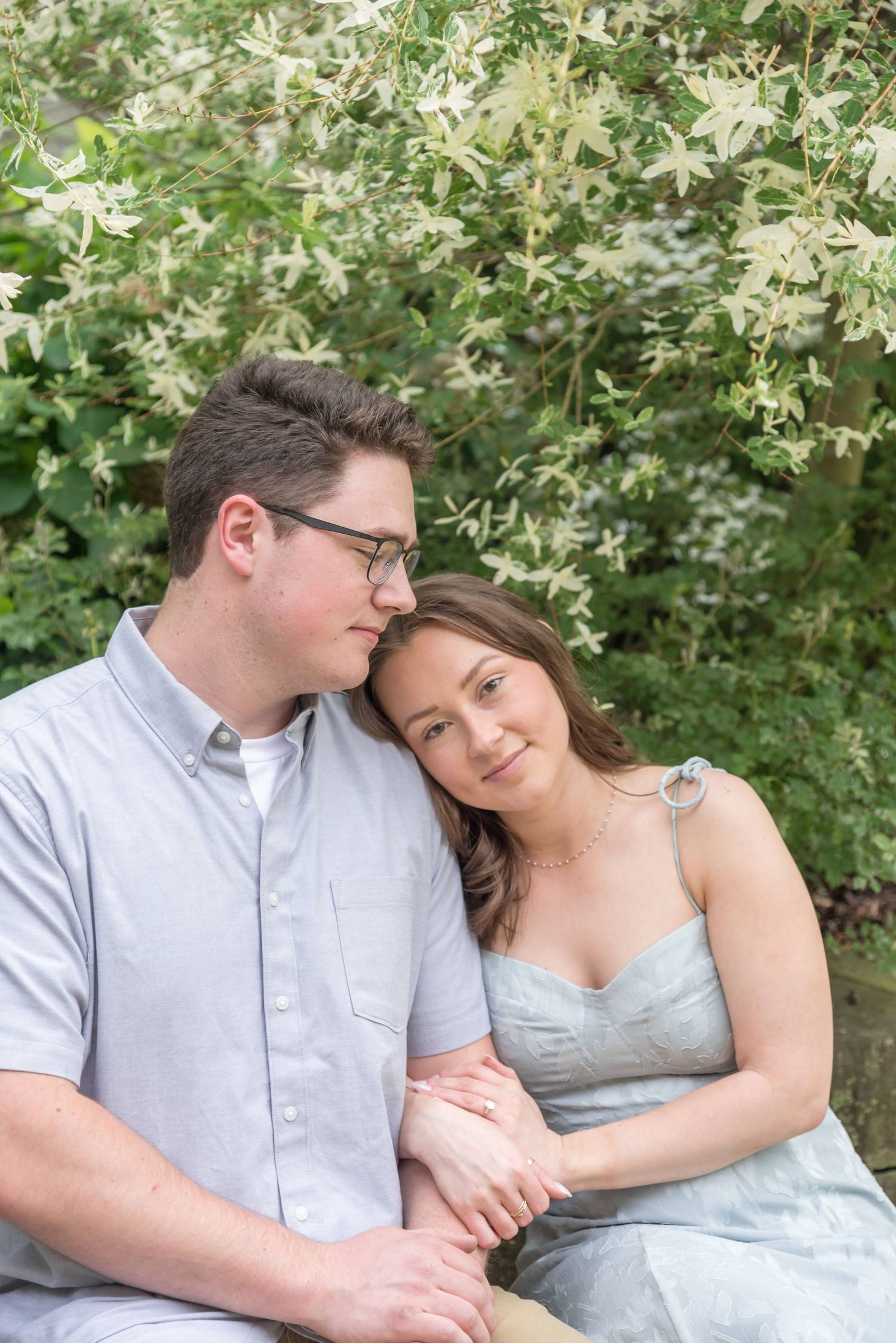 Romantic couple sitting close together among blooming white flowers.