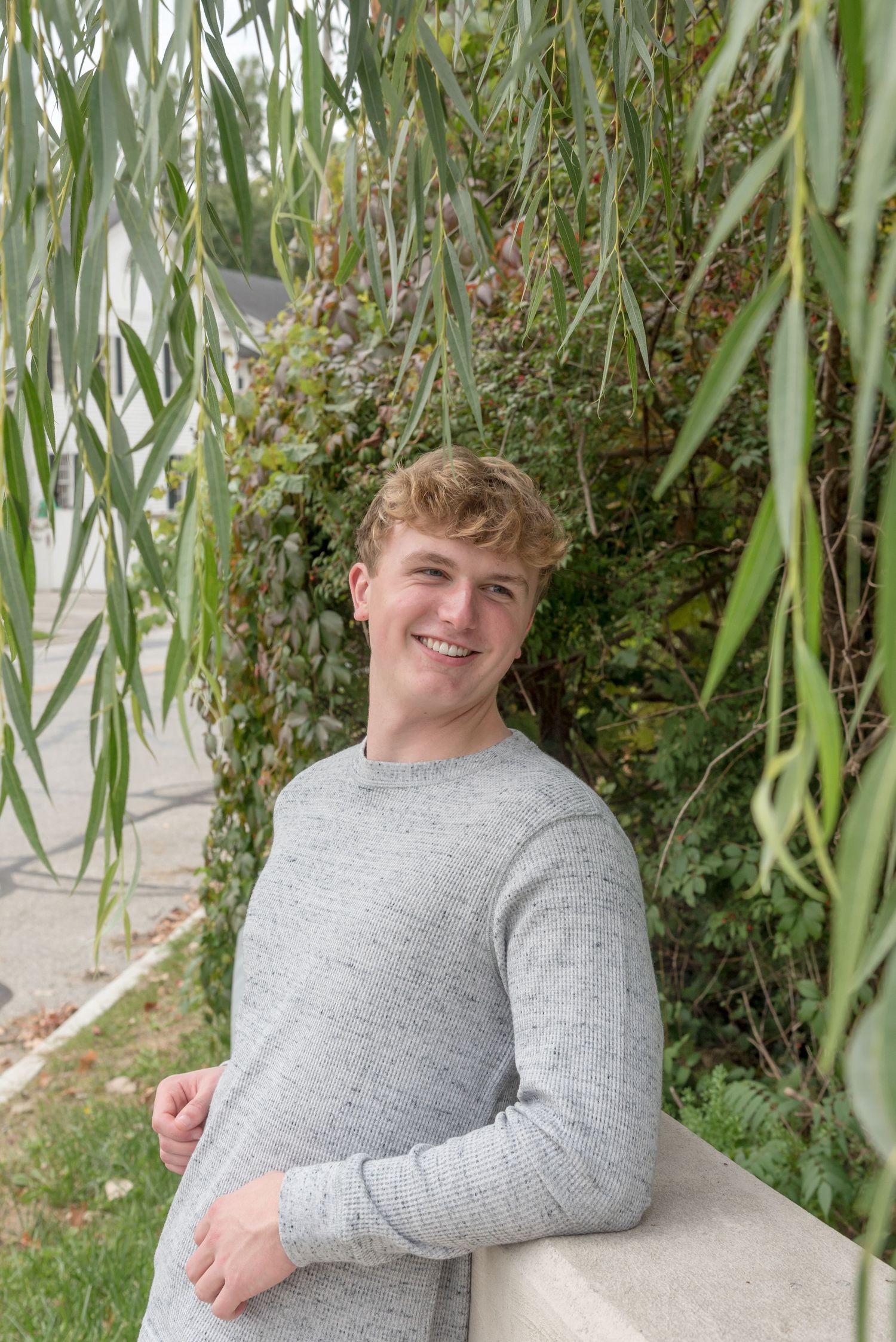 Person in grey sweater posing under willow tree branches.