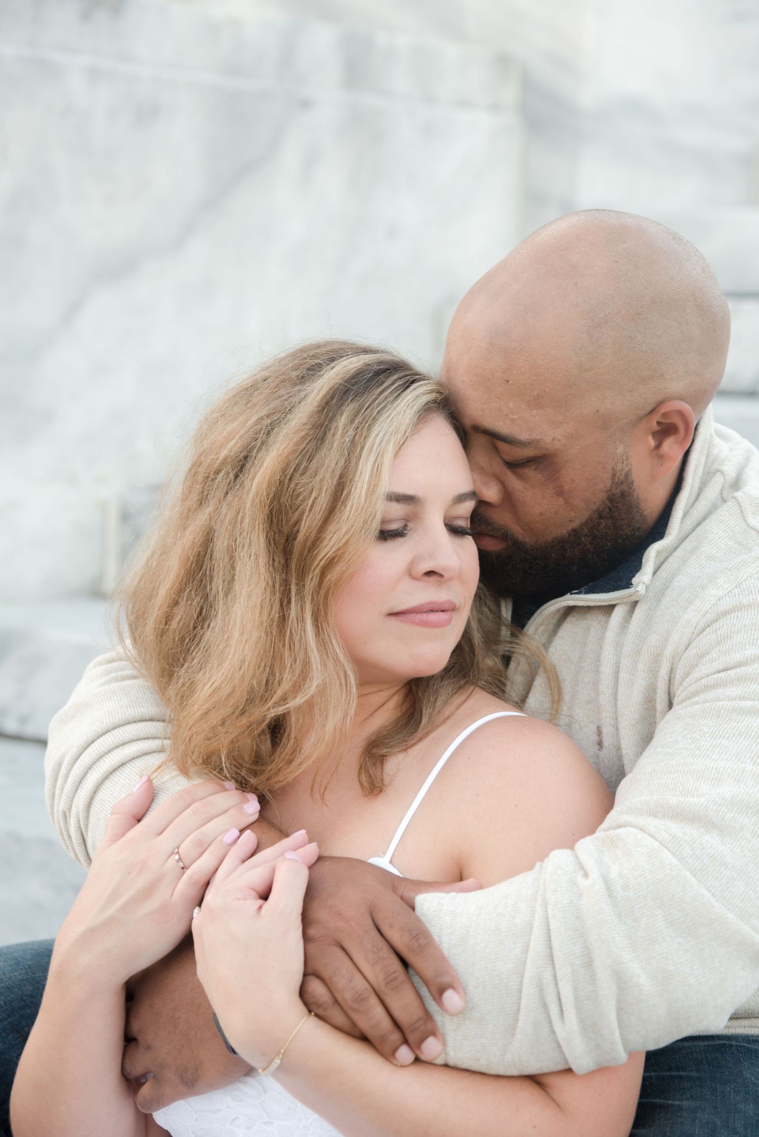Intimate couple portrait against white marble background.