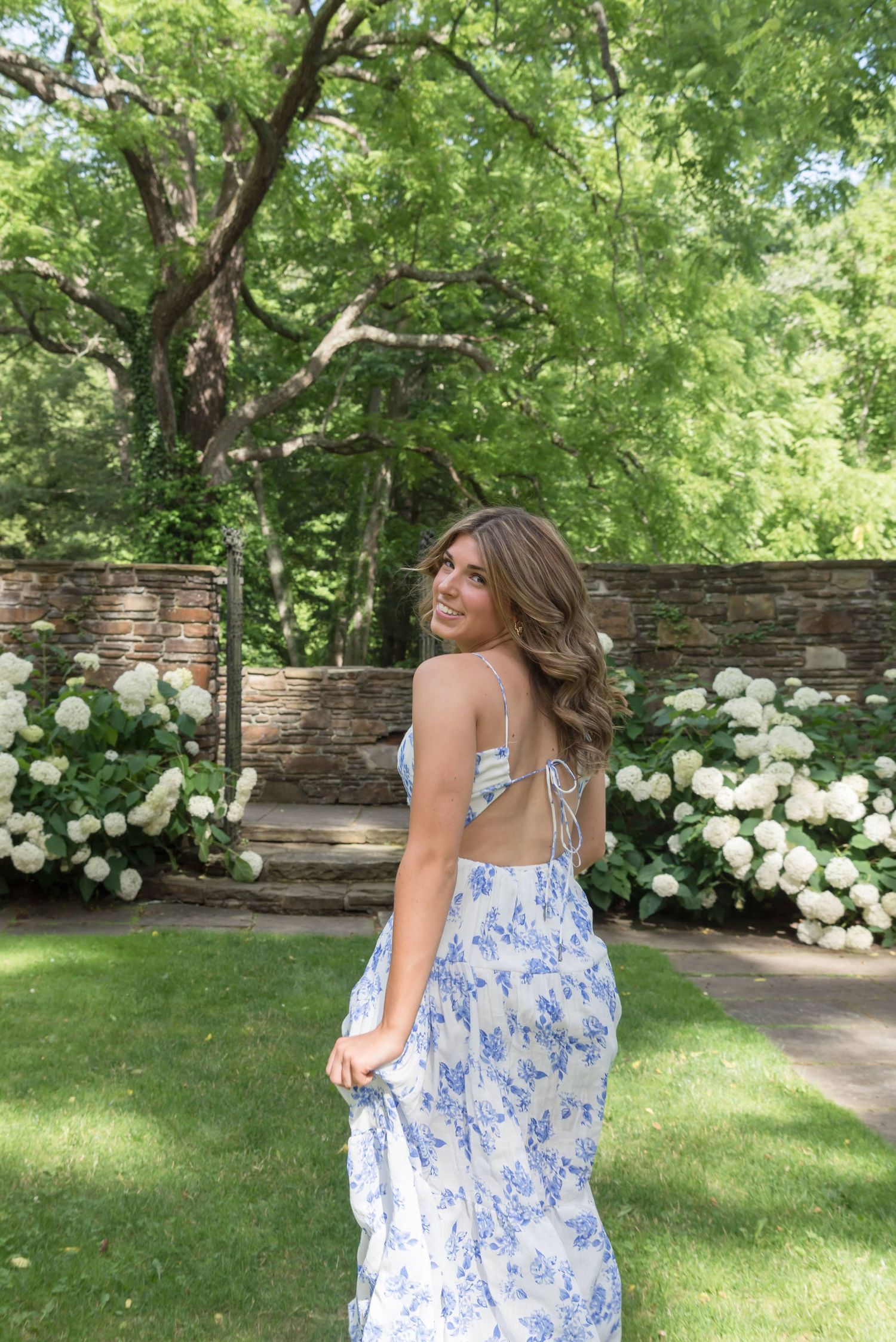 Person in flowing blue floral dress twirls in garden setting with white hydrangeas.