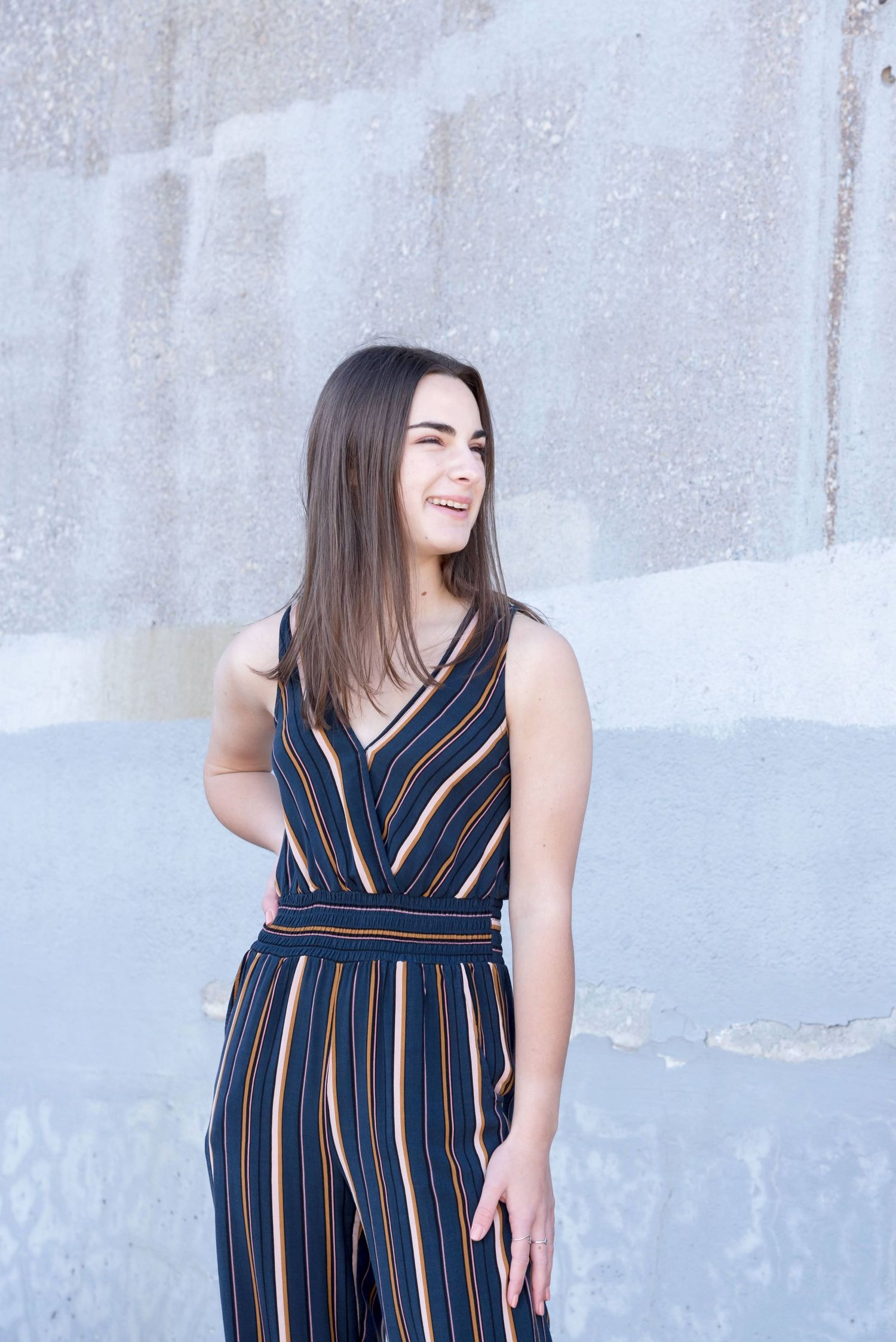 Person in striped navy jumpsuit poses against concrete wall.