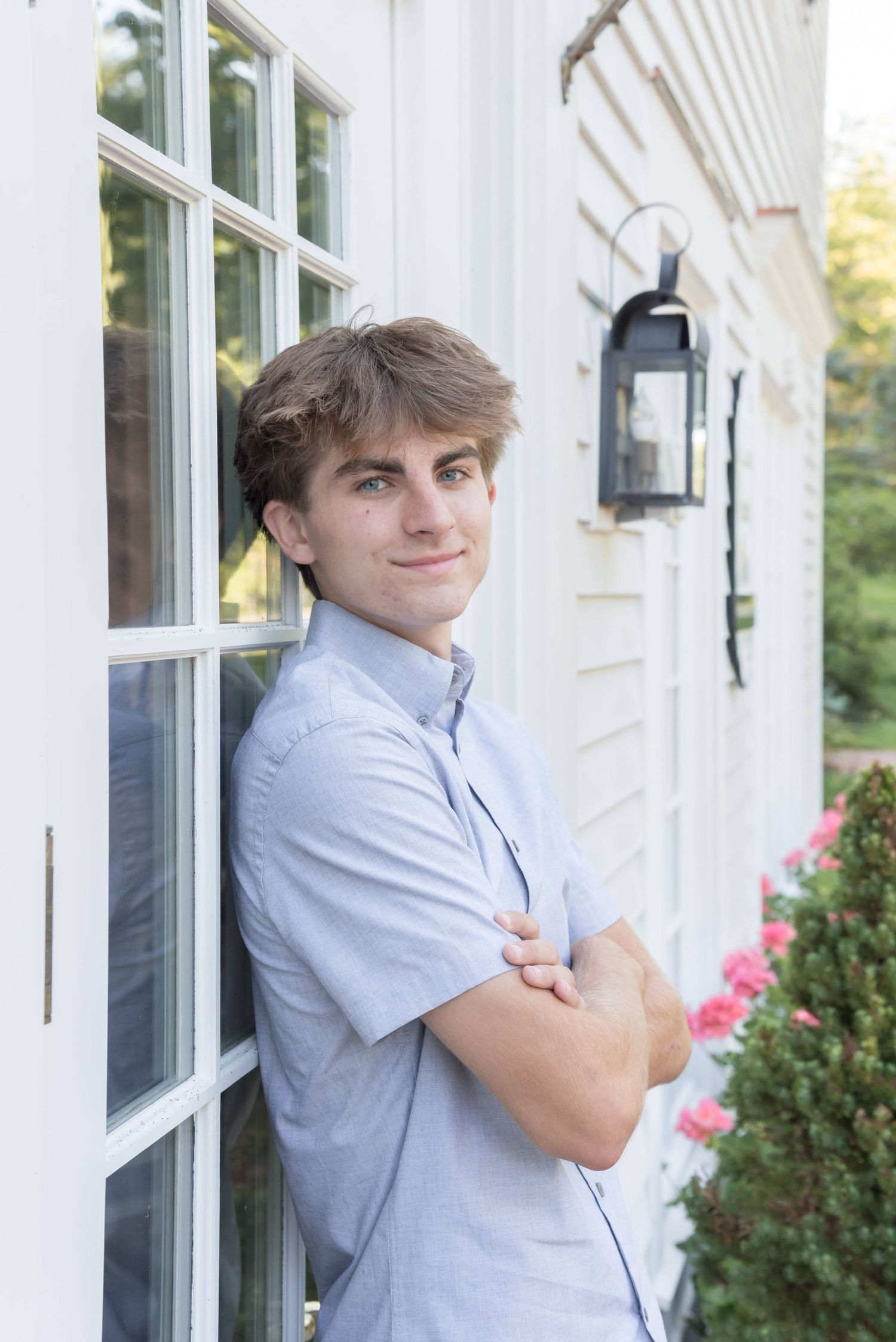 A person in a light blue button-down shirt poses against a white building exterior with a lantern.