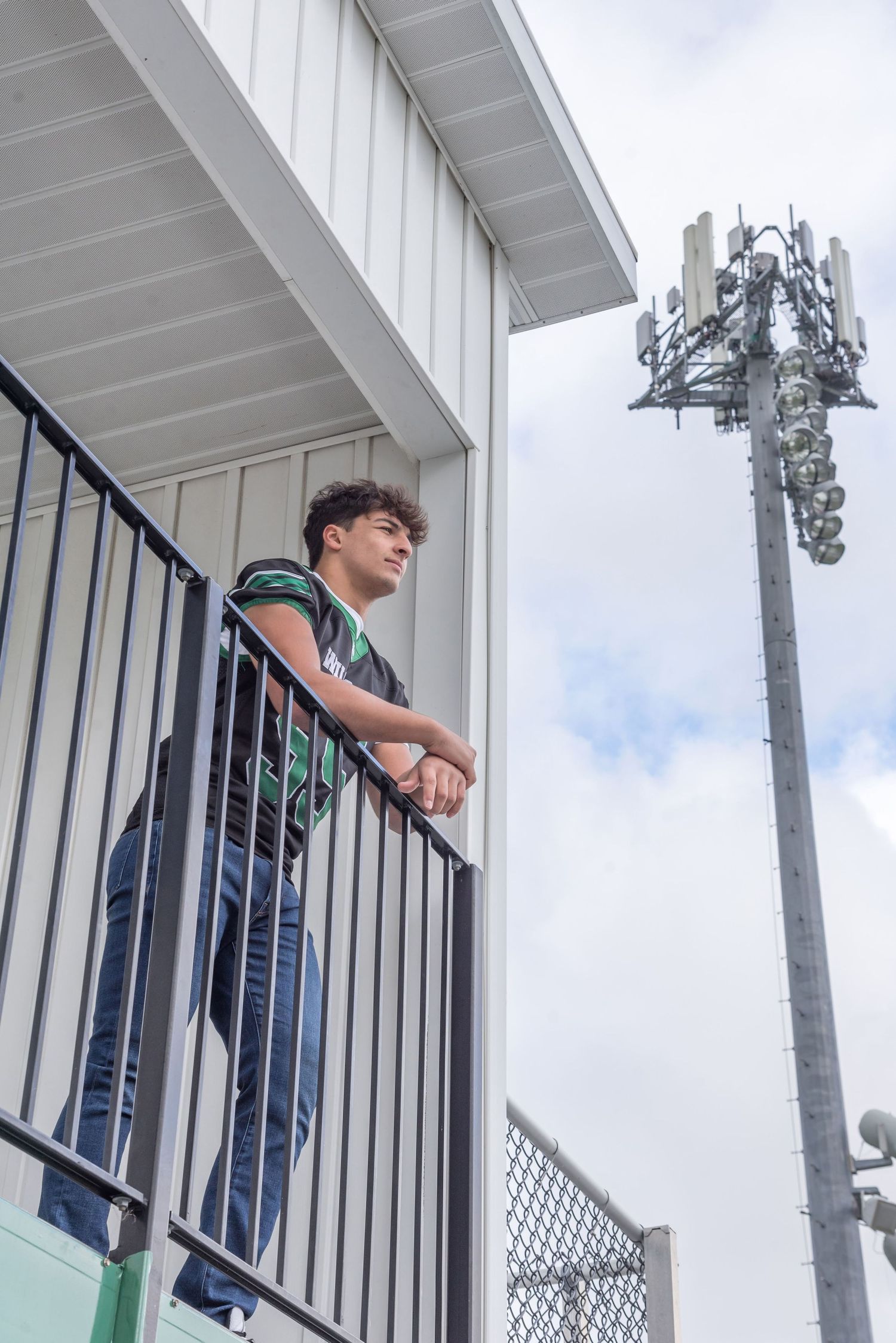 Person leaning on metal railing with cell tower visible in background.