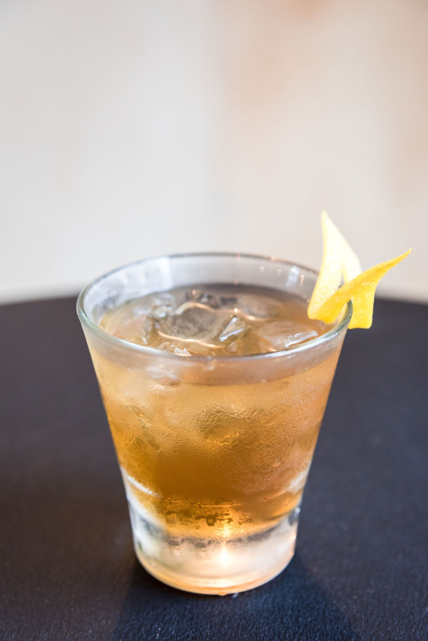 Amber-colored cocktail with citrus garnish served in glass bowl.
